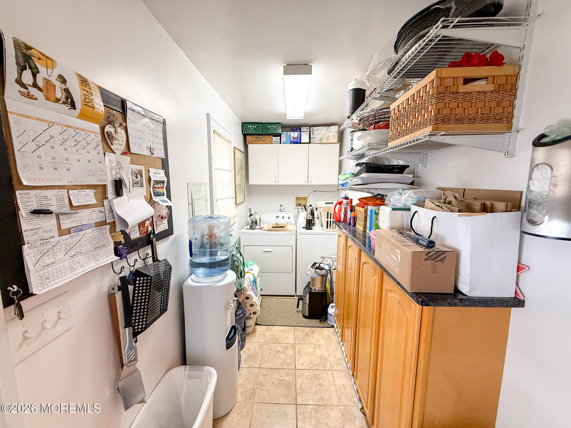 Utility room with laundry appliances, a water cooler, wall cabinets, and extensive storage shelving.