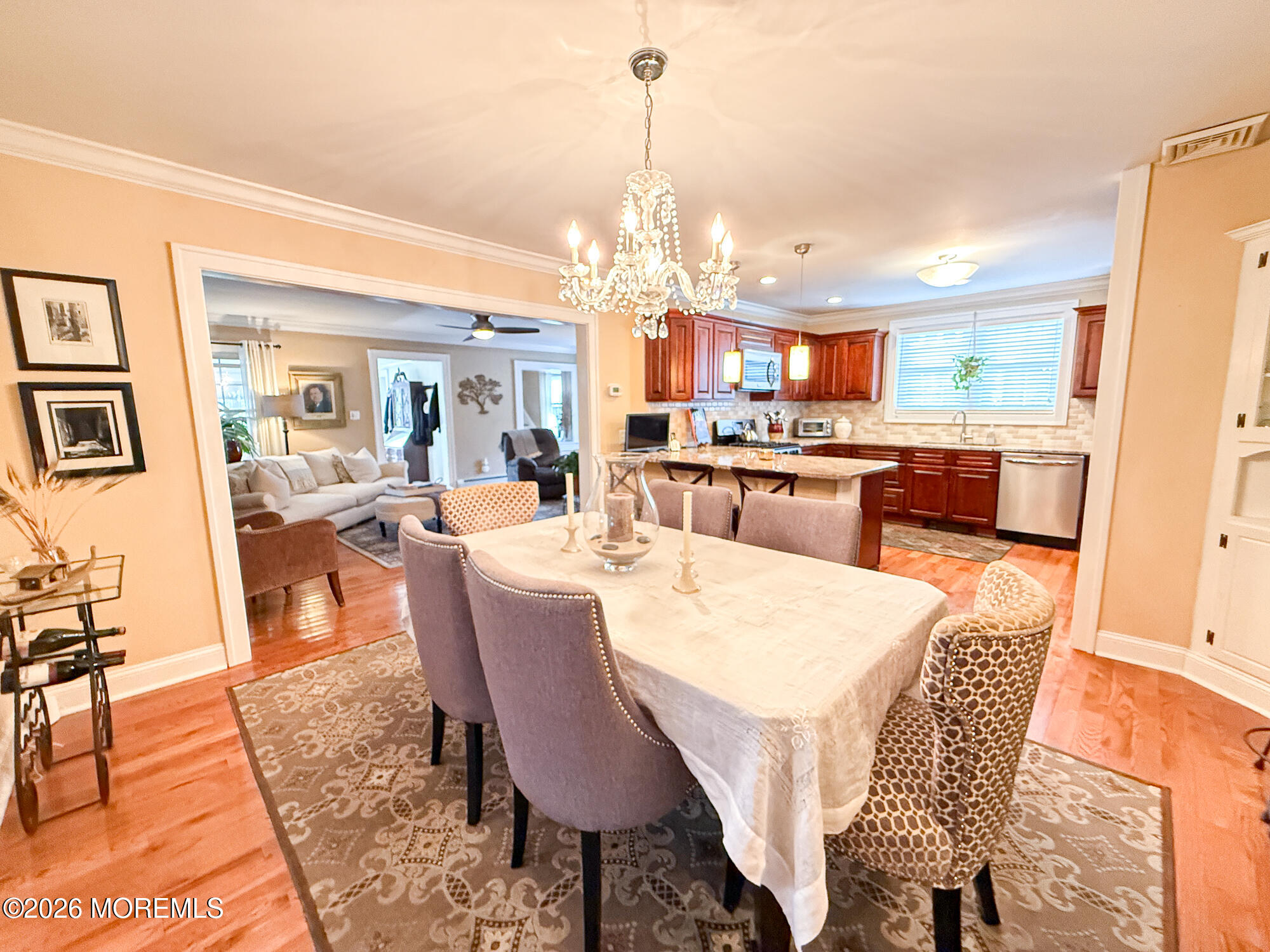 Dining room with chandelier and long table opening onto a living room and dark wood kitchen.