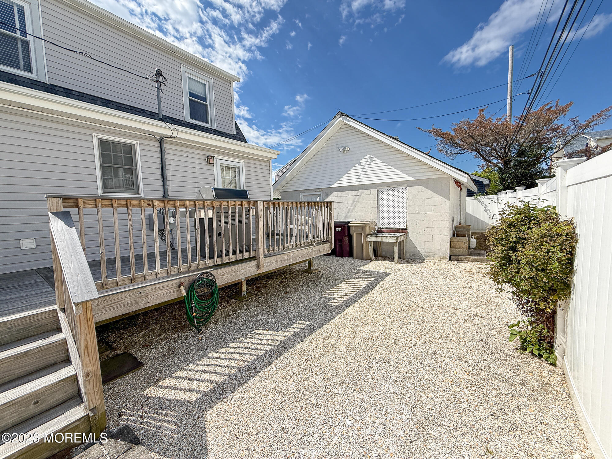 Backyard with a gravel yard, raised wooden deck, detached outbuilding, and white privacy fence.