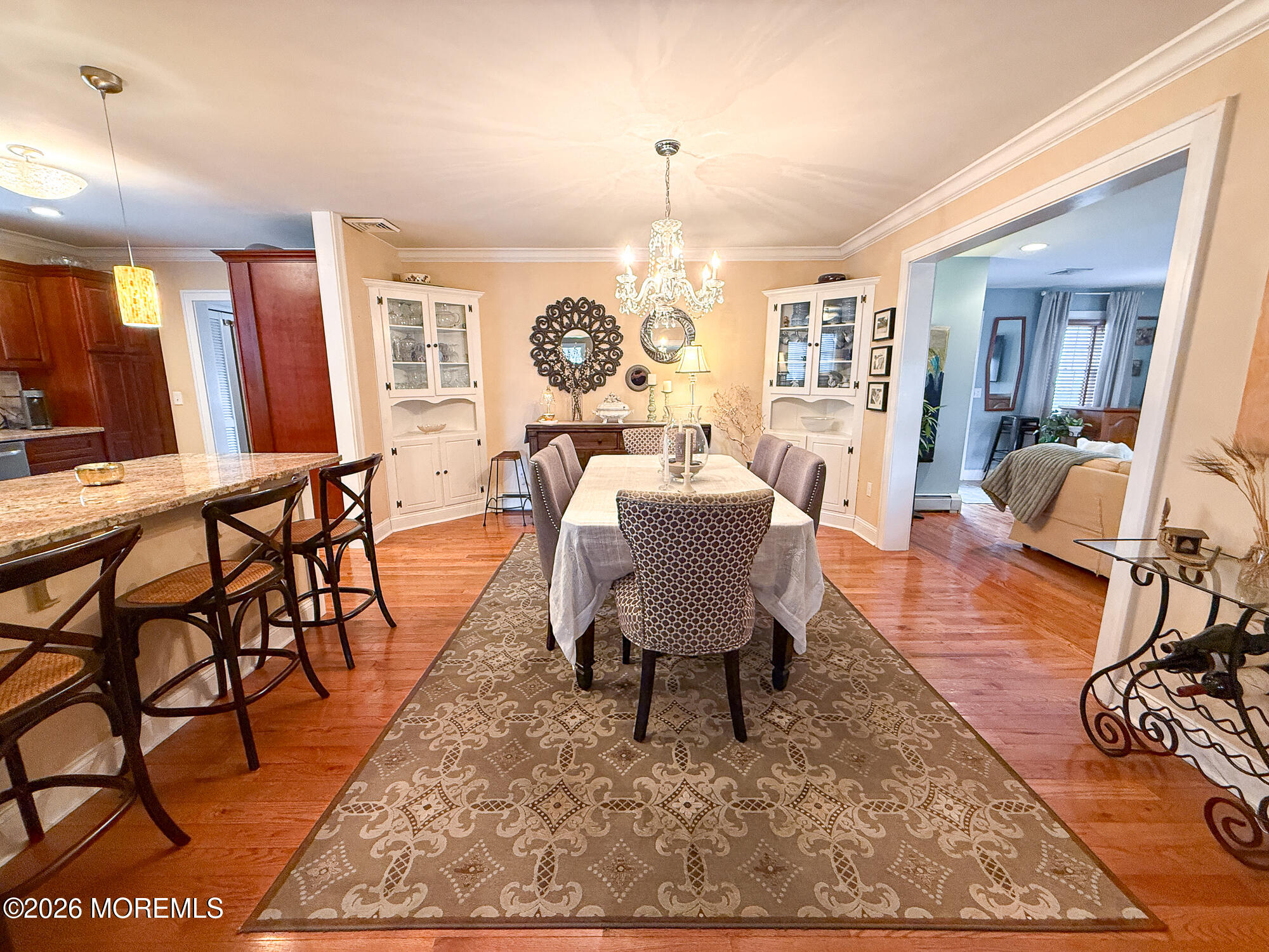 Furnished dining room with a chandelier, white china cabinets, patterned rug, and adjoining sitting room.