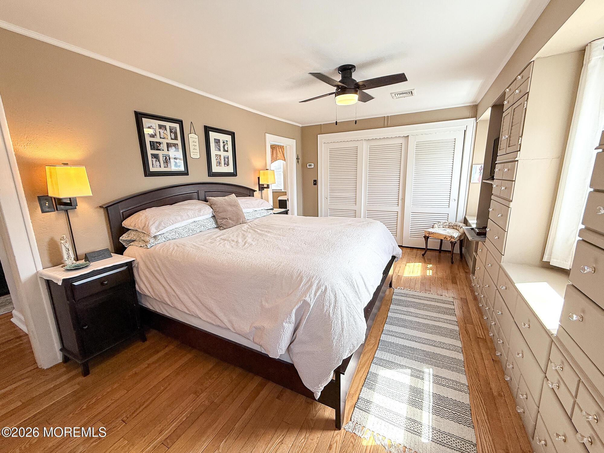Furnished bedroom with a large bed, hardwood floors, and built-in drawers along one wall.