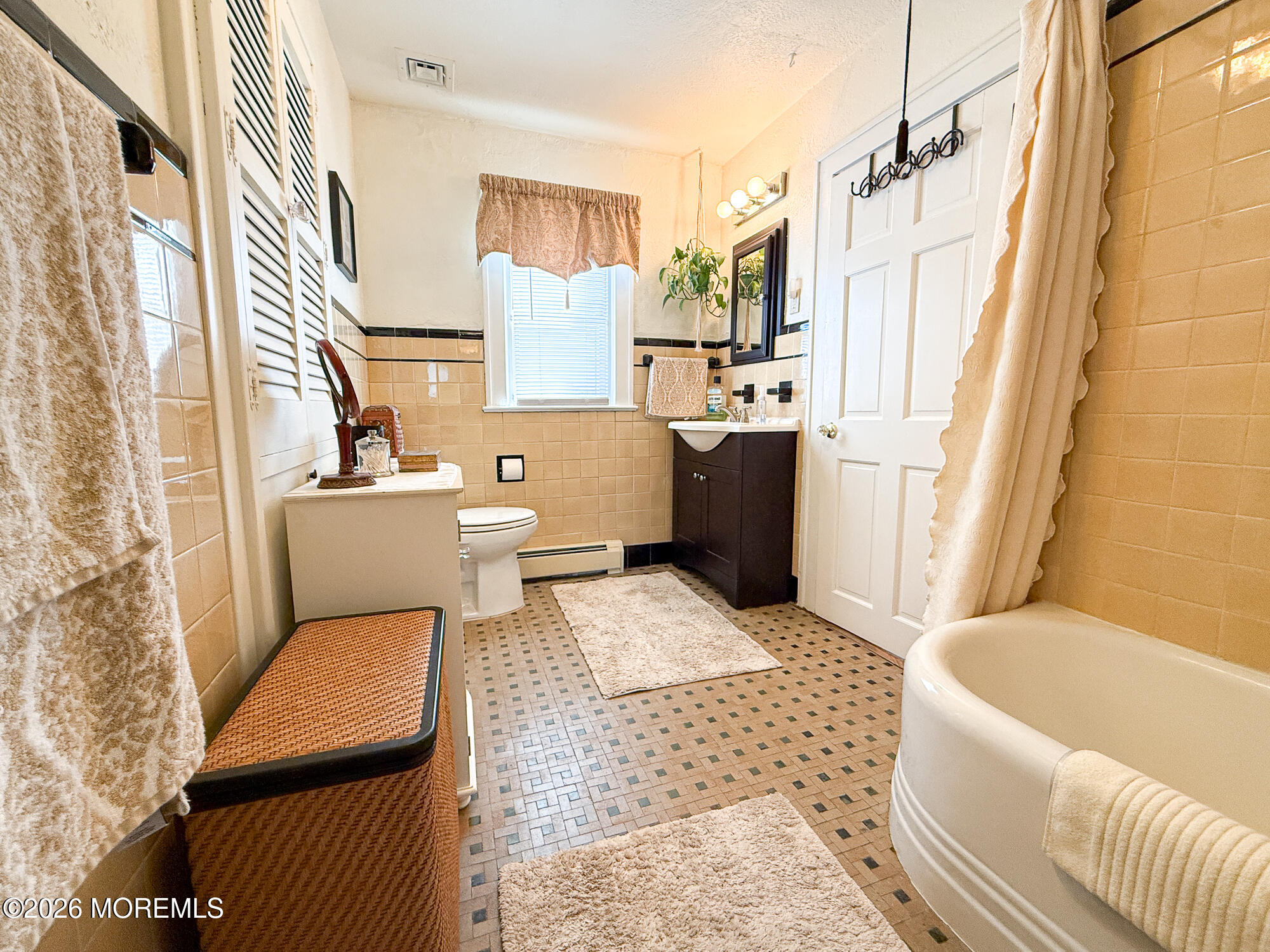 Bathroom with a white clawfoot-style tub, beige tile, mosaic floor, and dark vanity.