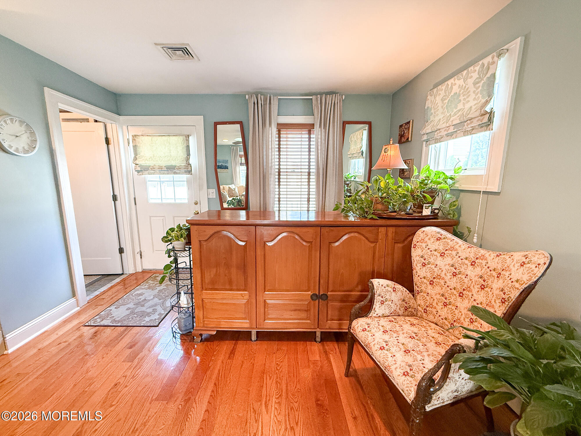 Furnished entryway with polished hardwood floors, a wooden console cabinet, and a floral chair.