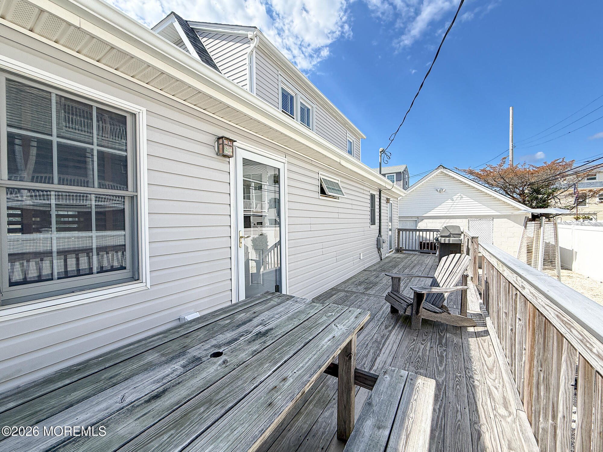 Wooden deck with Adirondack chairs and a grill beside the home.