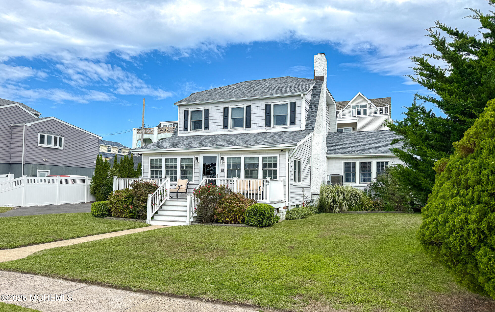 White two-story house with a covered porch, white railings, and landscaped front lawn.