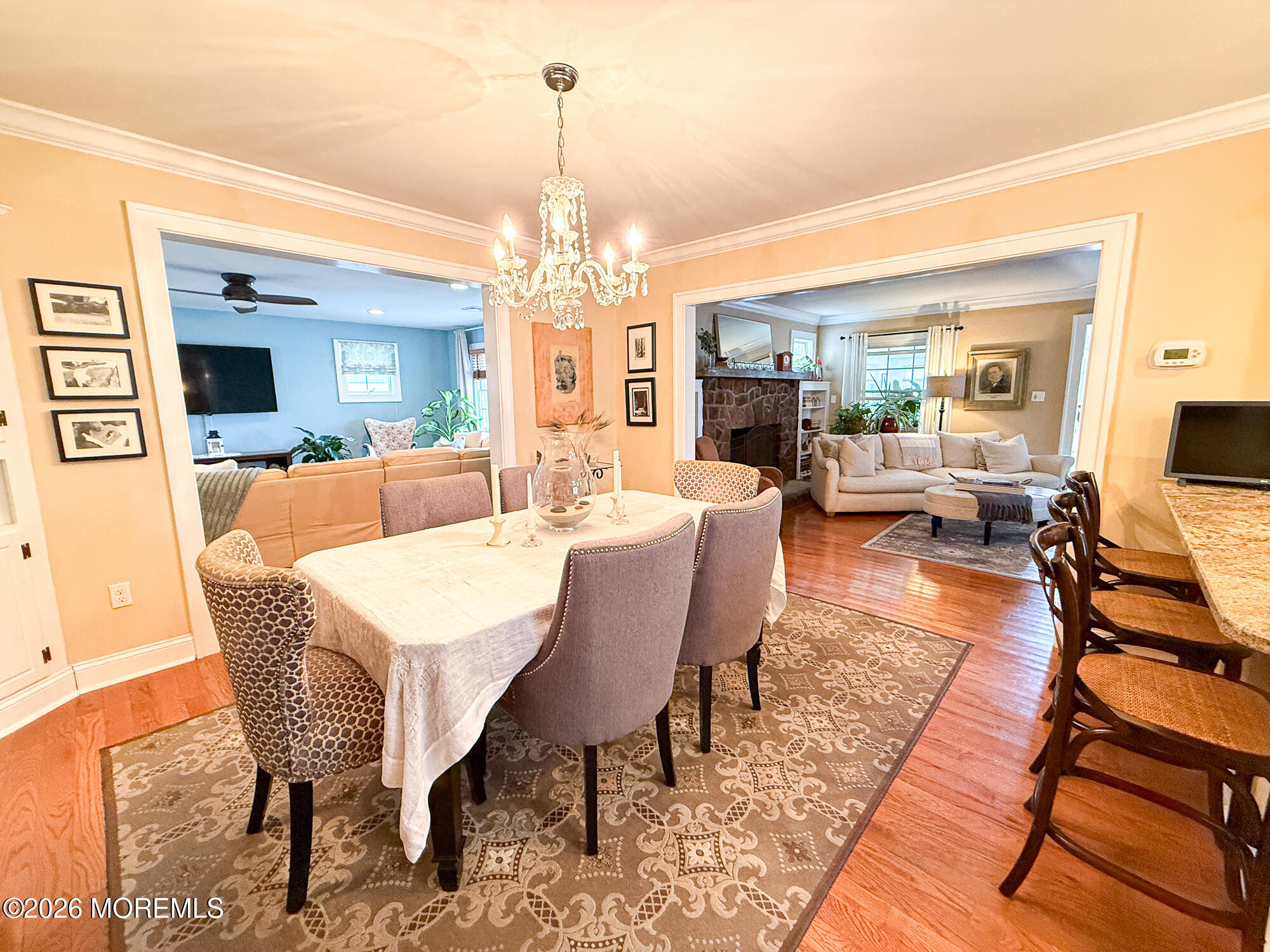 Dining room with a chandelier and patterned rug, opening onto two furnished living areas.