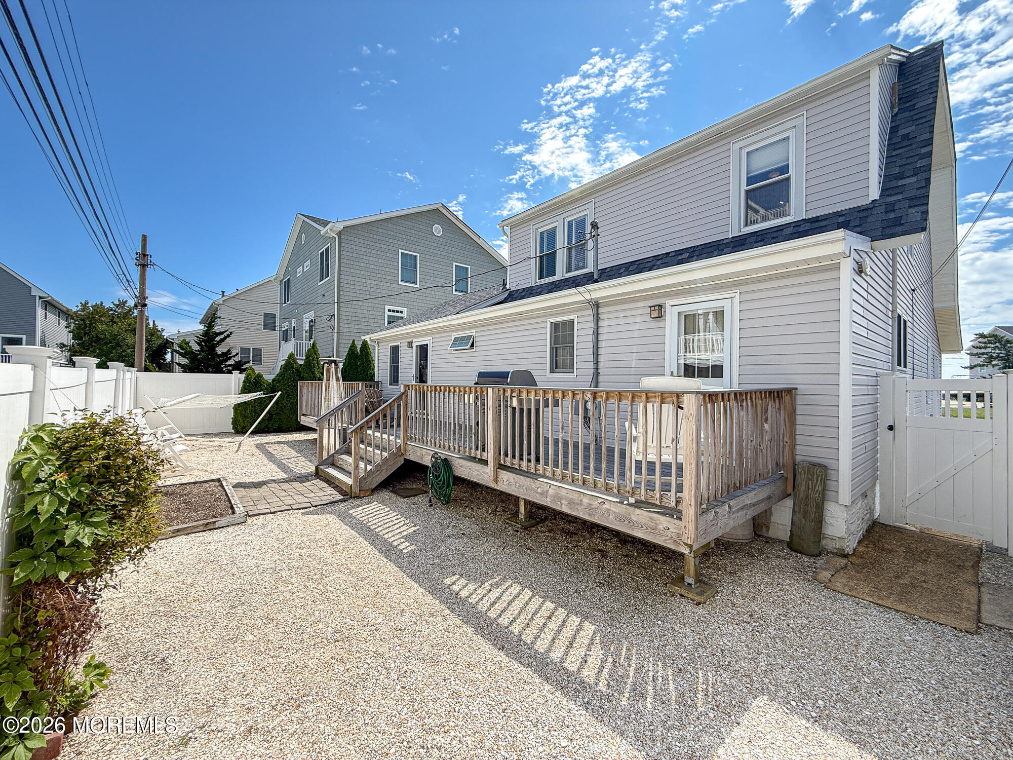 House exterior with raised wooden deck, gravel yard, white fencing, and outdoor chairs.