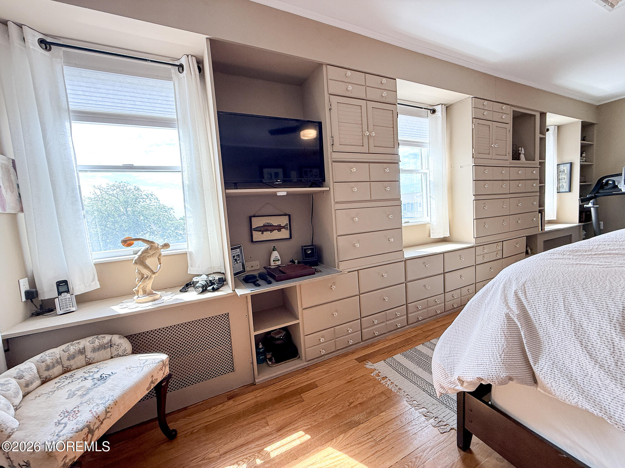 Bedroom with extensive built-in cabinetry, a wall-mounted TV, and windows overlooking water.
