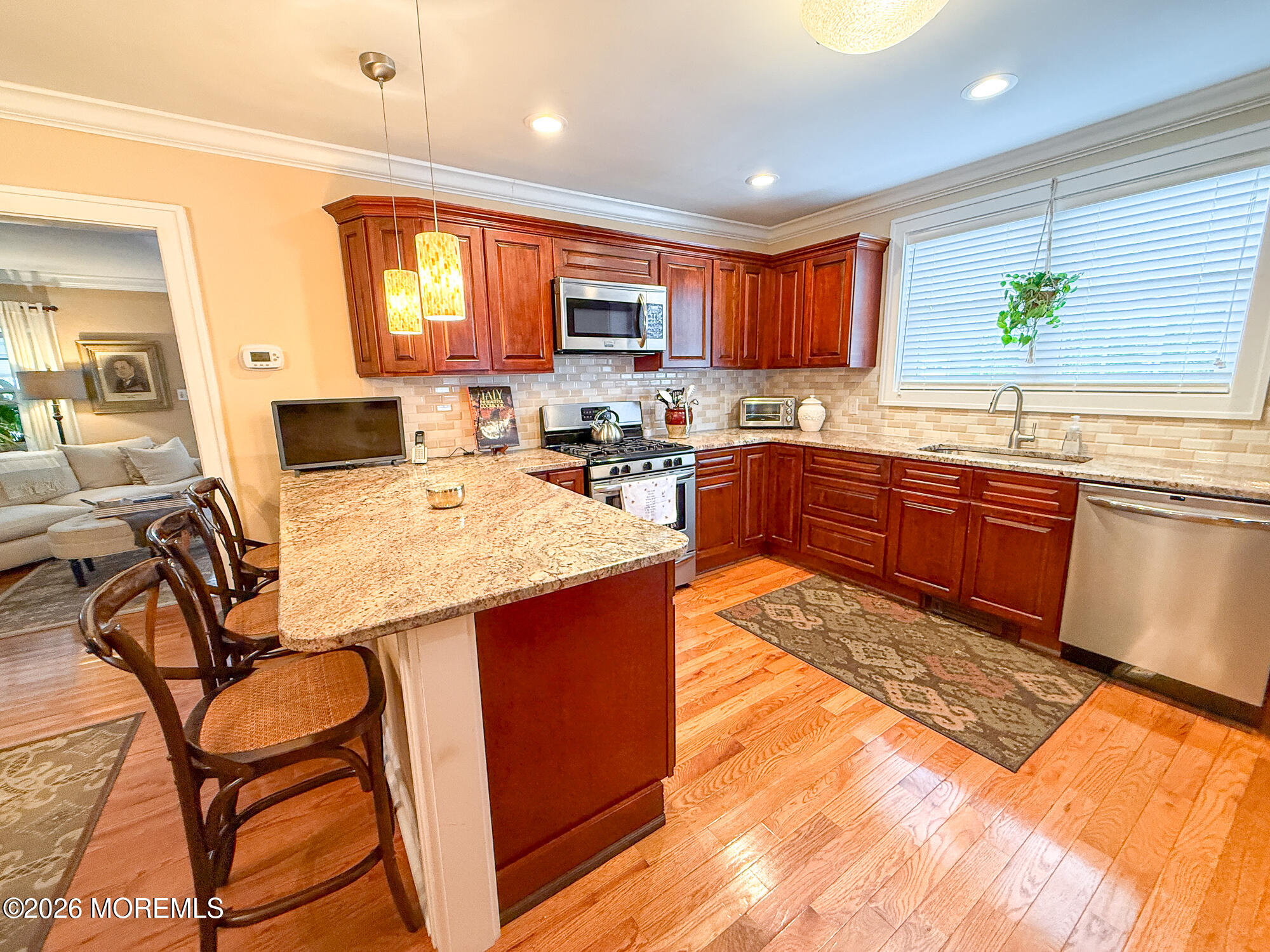 Kitchen with reddish-brown cabinets, granite breakfast bar, stainless steel appliances, and hardwood floors.