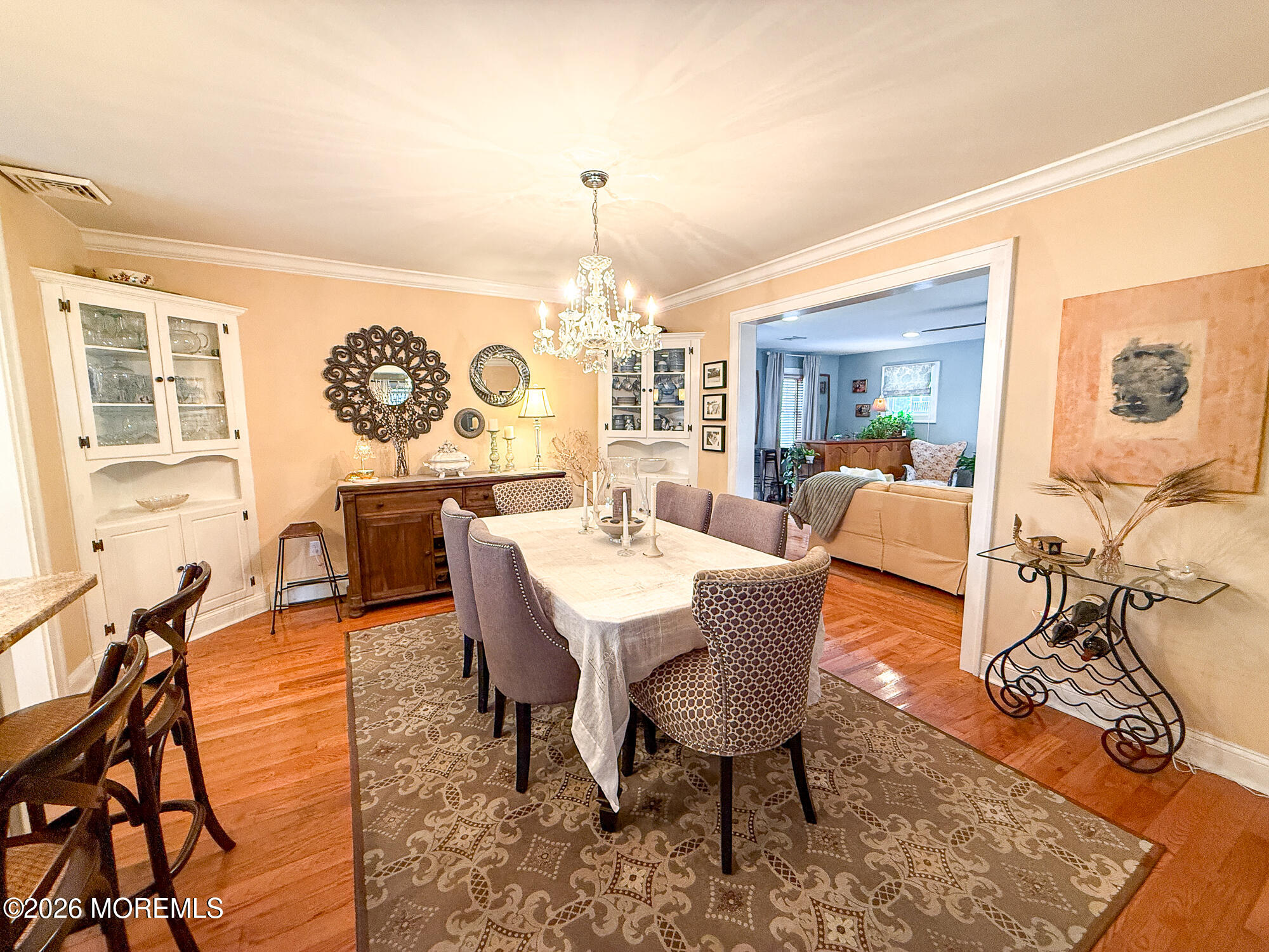 Dining room with a crystal chandelier, built-in cabinets, patterned rug, and adjoining living room.