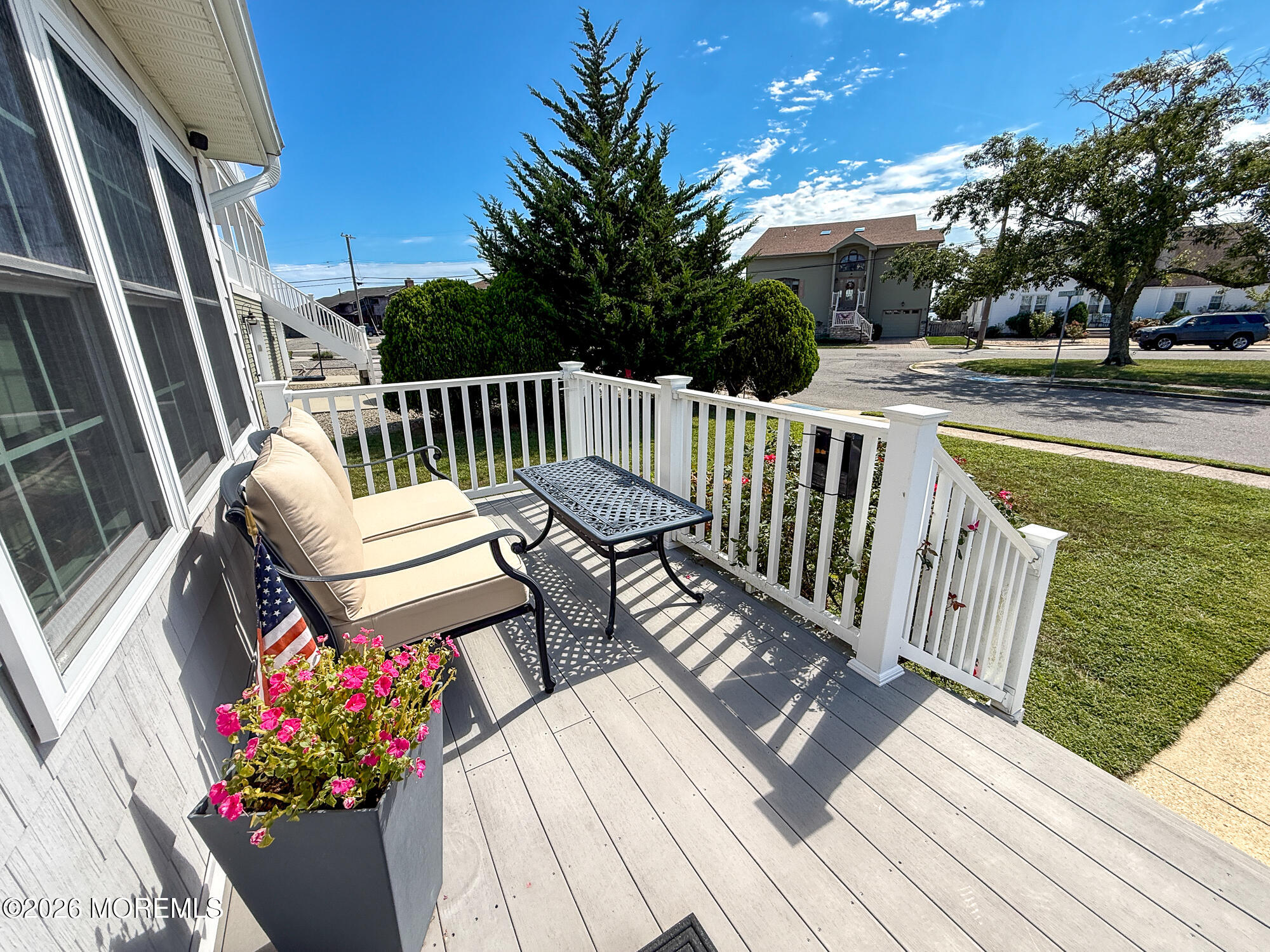 Front porch deck with cushioned seating, white railings, and a planter of pink flowers.