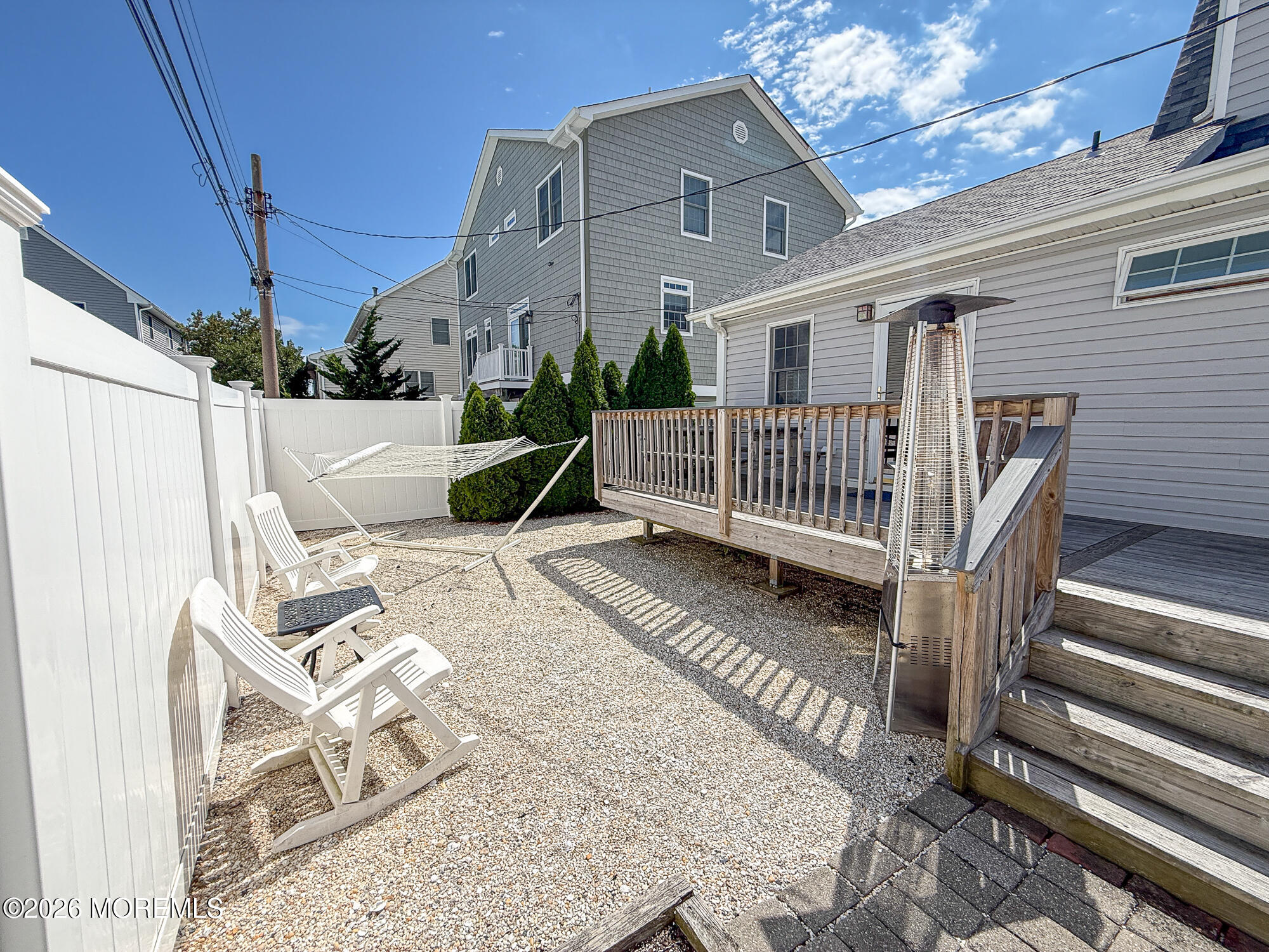 Gravel backyard patio with Adirondack chairs, hammock, and raised wooden deck.