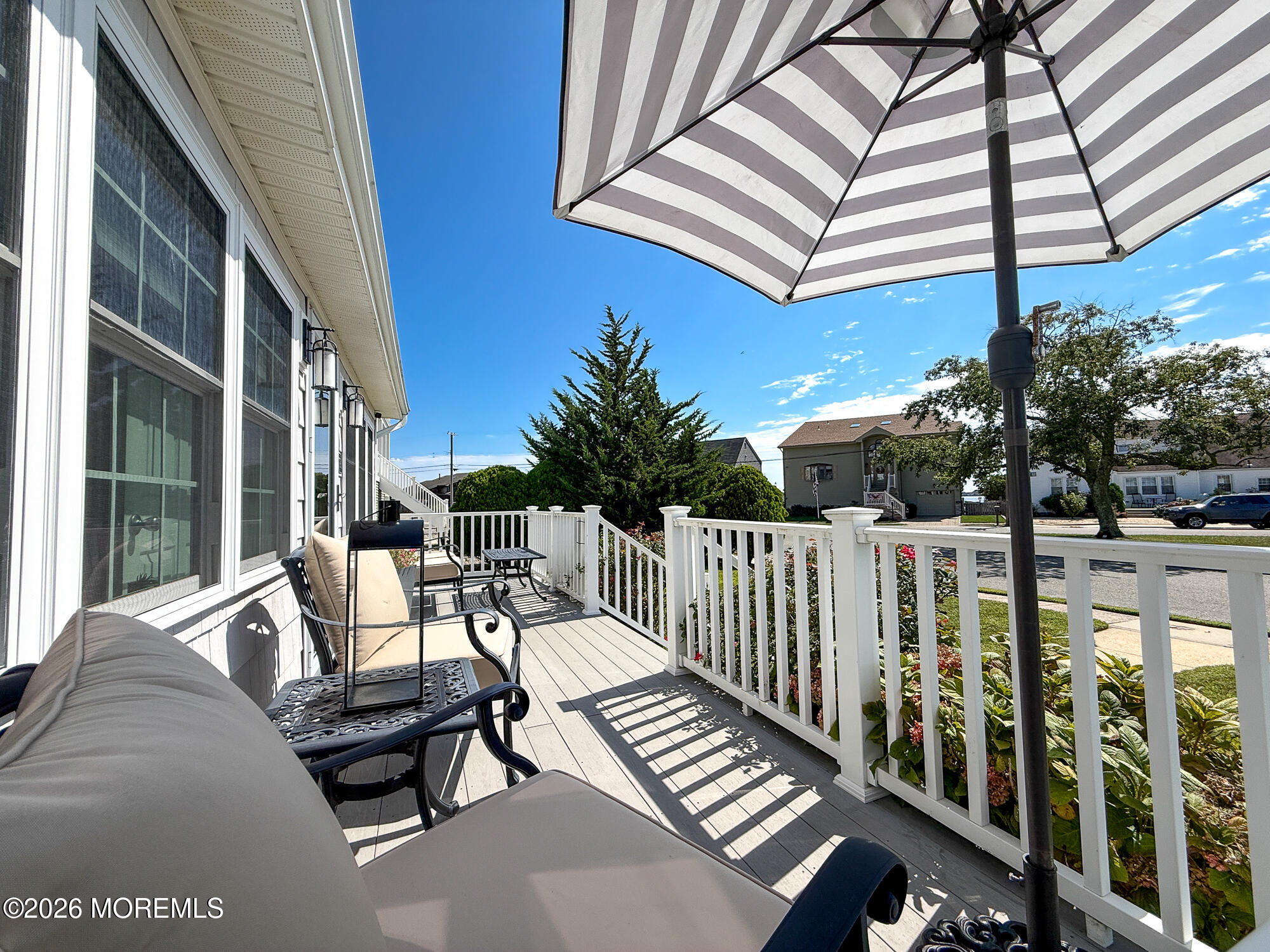 Furnished porch with white railings, cushioned chairs, and a large striped umbrella.