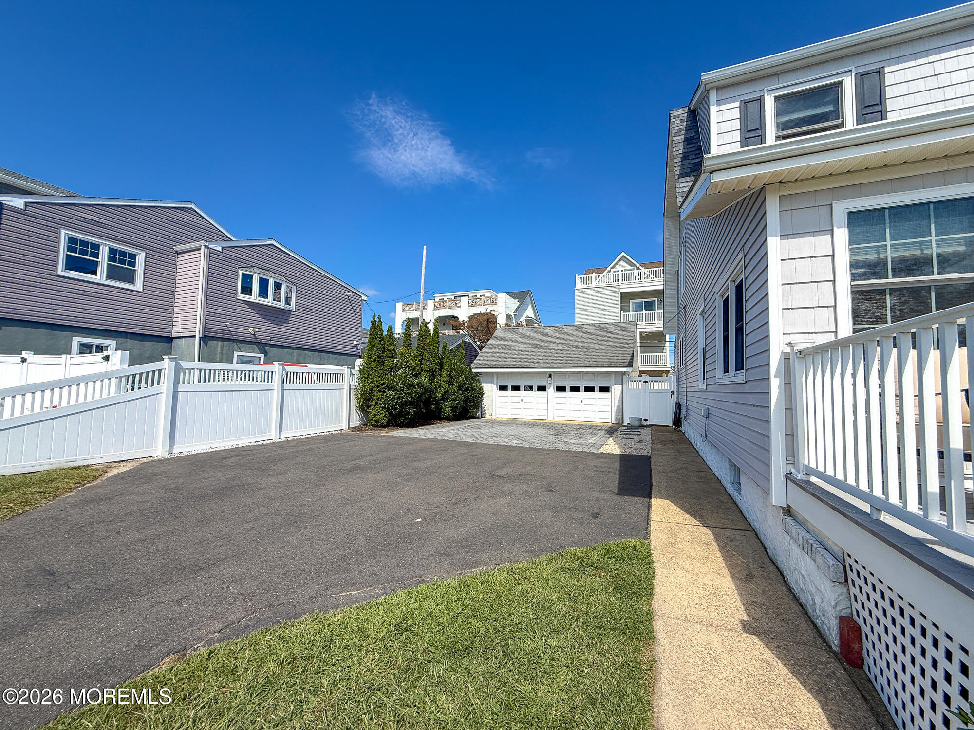 House exterior beside a wide asphalt driveway leading to a detached double garage, with white fencing.