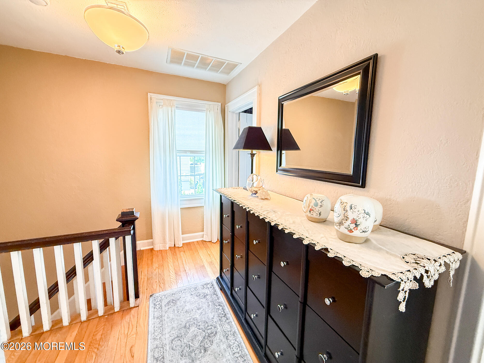 Upstairs landing with wood floors, a dark console and mirror beside a curtained window and staircase.