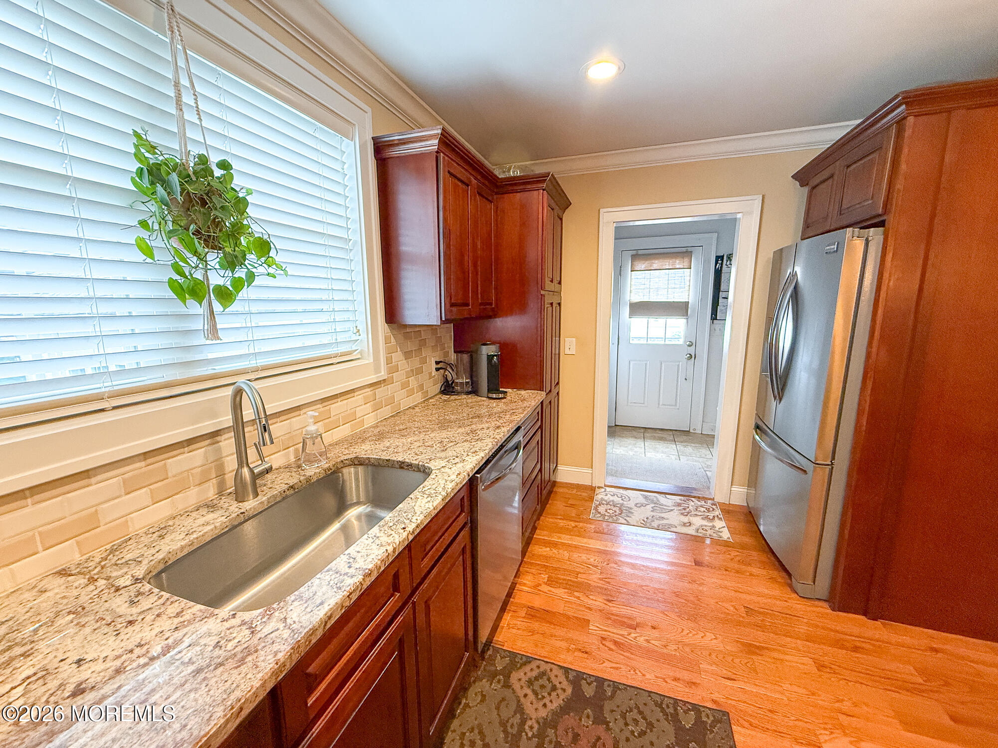 Kitchen with cherry cabinets, granite counters, a window-side sink, stainless steel appliances, and hardwood floors.