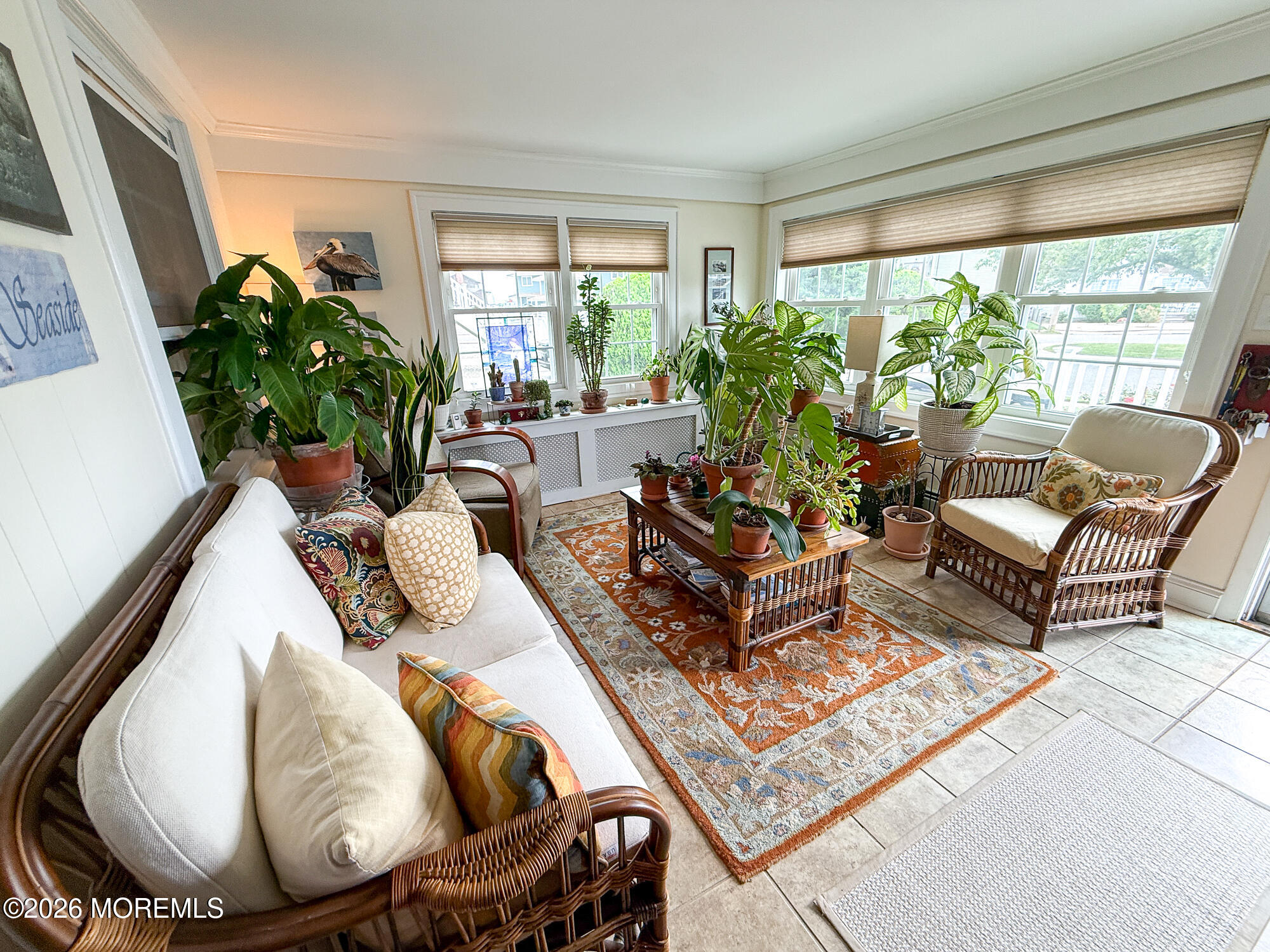 Sunroom with wicker seating, a patterned rug, and potted plants by large windows.