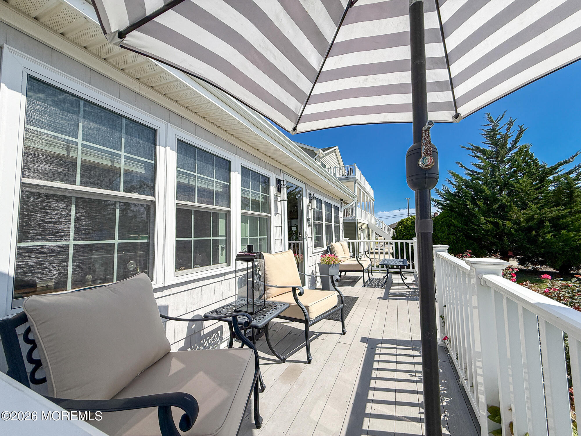 Furnished raised deck with cushioned chairs, a striped umbrella, and white railings.