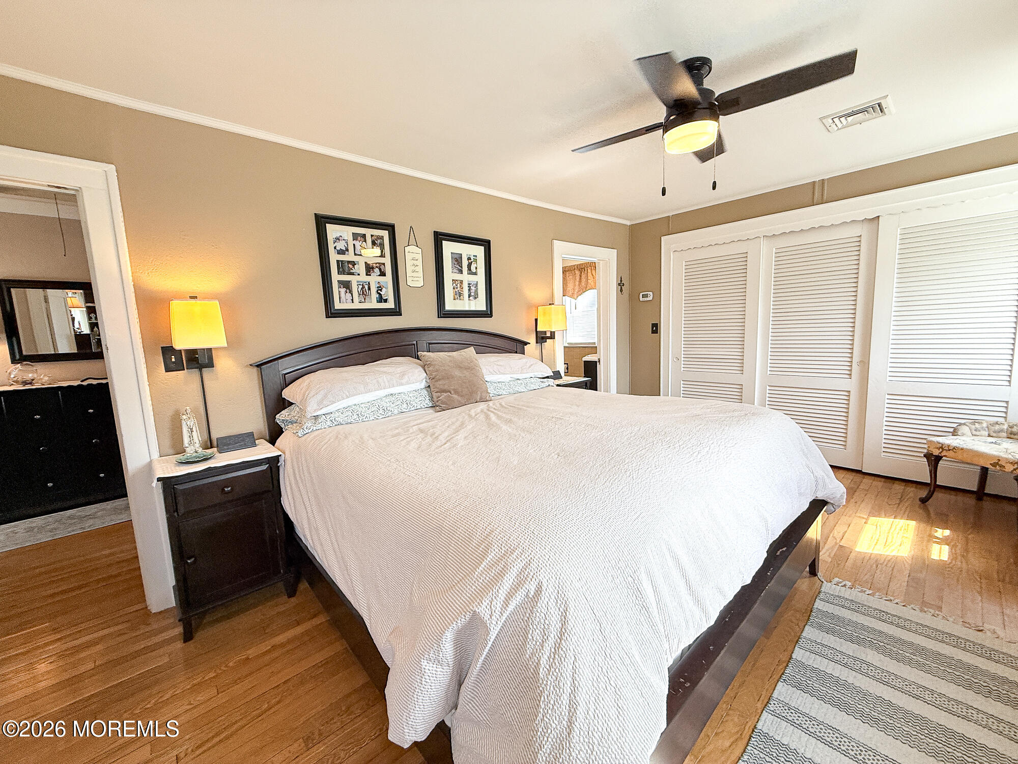 Furnished bedroom with a large bed, hardwood floors, louvered closet doors, and ceiling fan.