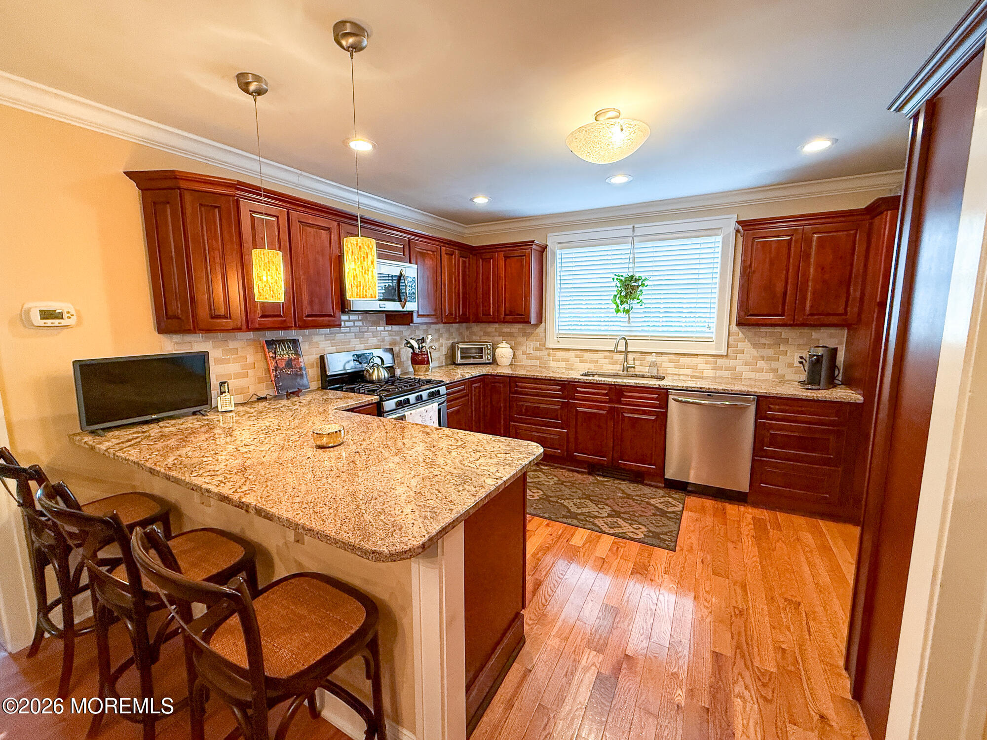 Kitchen with cherry cabinets, granite breakfast bar, stainless steel appliances, and hardwood floors.