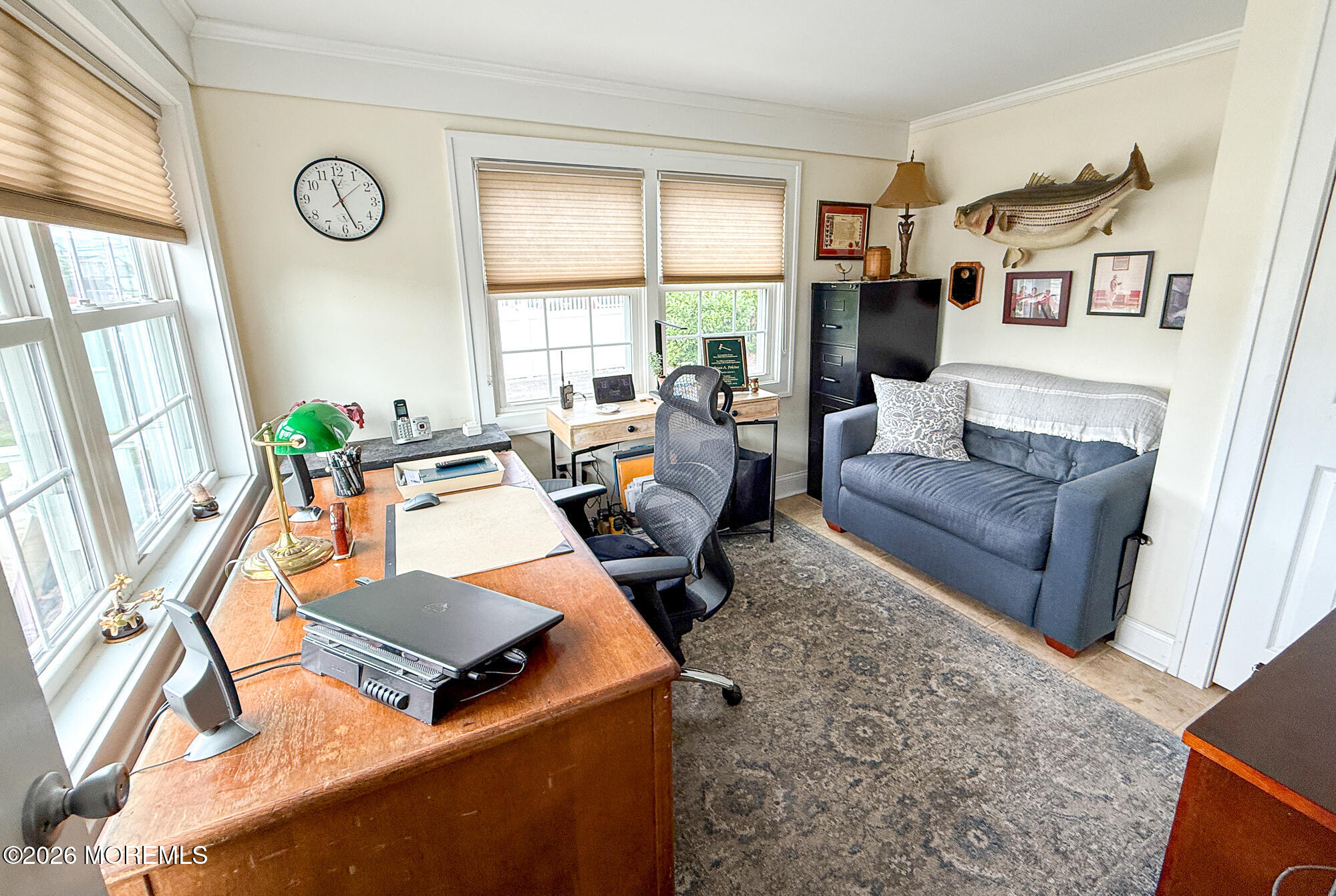 Home office with a large wooden desk, gray sofa, and mounted fish decor.