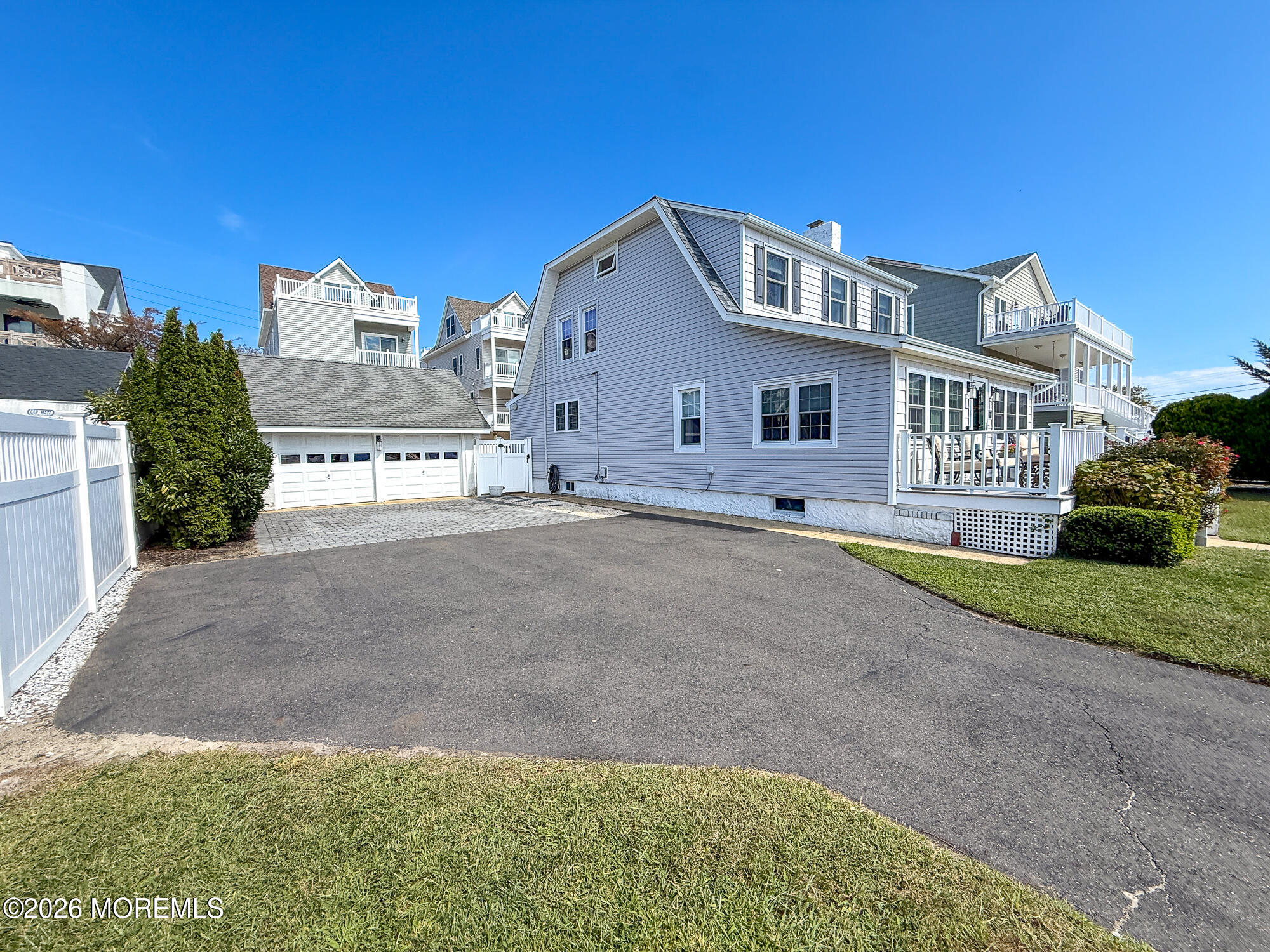 Gray coastal-style house with a white-railed deck, two-car garage, and wide paved driveway.