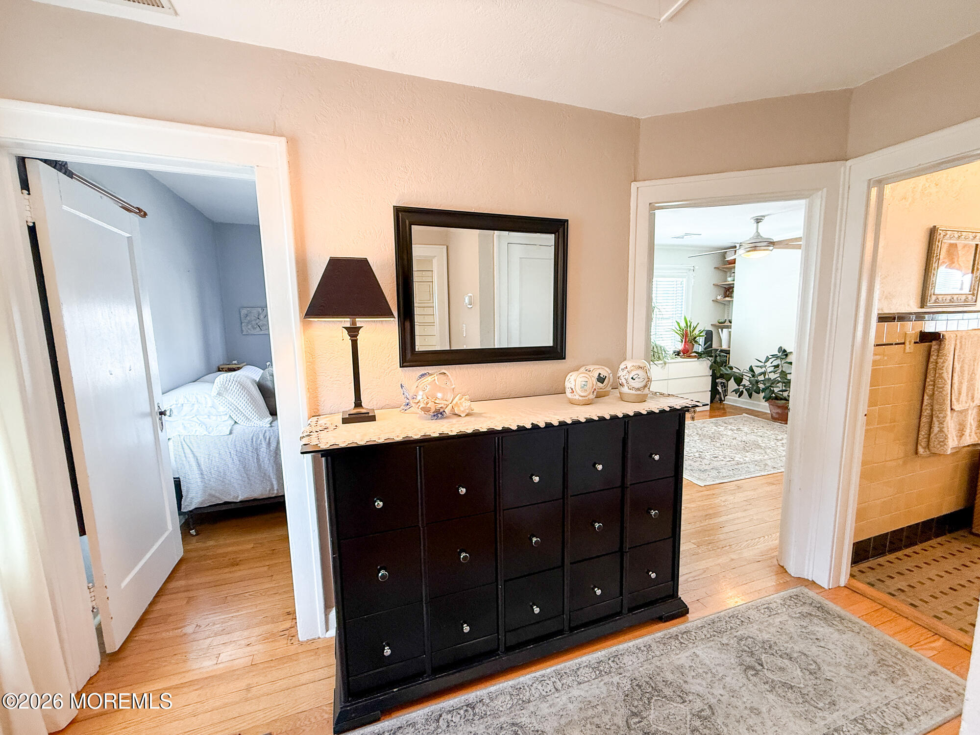 Furnished hallway with a dark dresser and mirror, opening to a bedroom and bathroom.