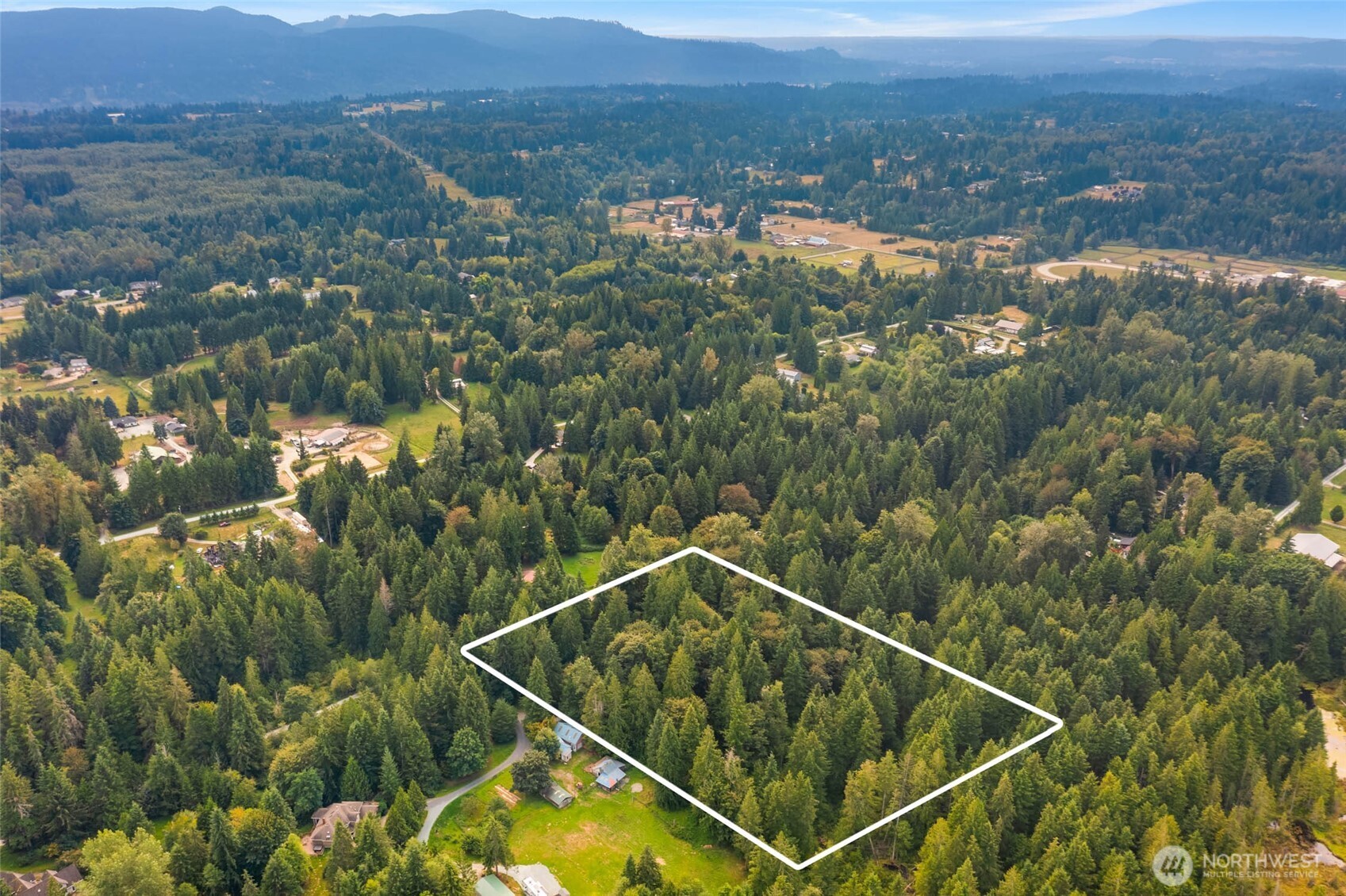 Aerial view of a forested parcel outlined in white, with distant mountain ranges.