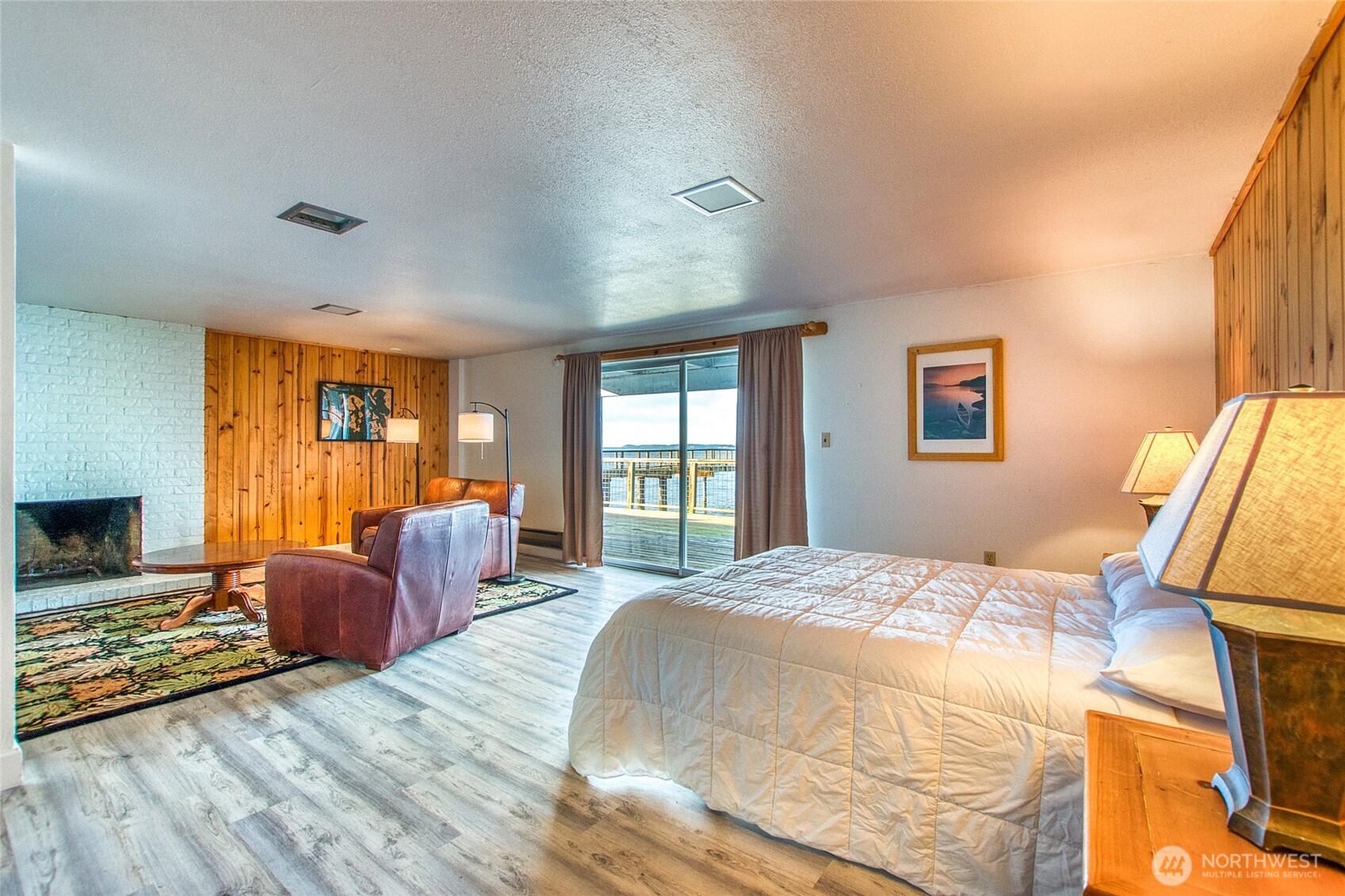 Furnished bedroom with a white brick fireplace and sliding doors overlooking the water.