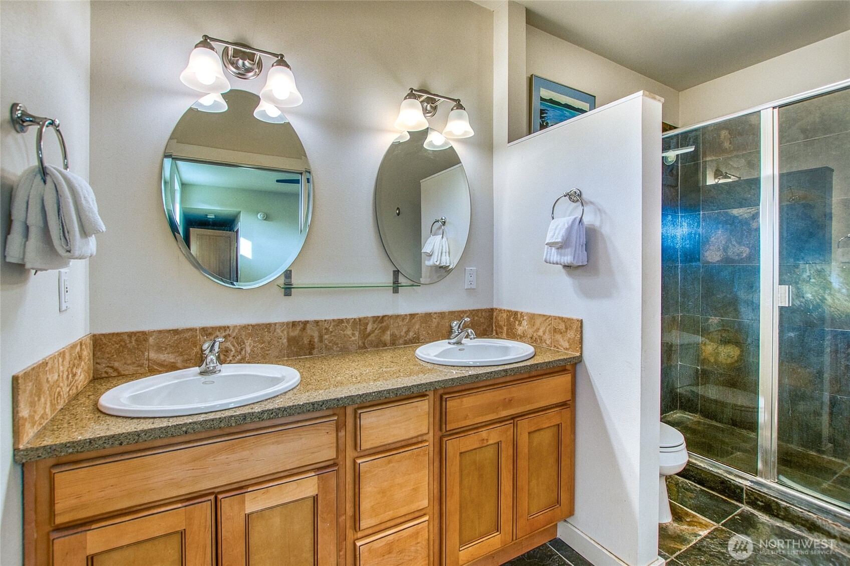 Bathroom with a double-sink vanity, oval mirrors, and a glass-enclosed tiled shower.