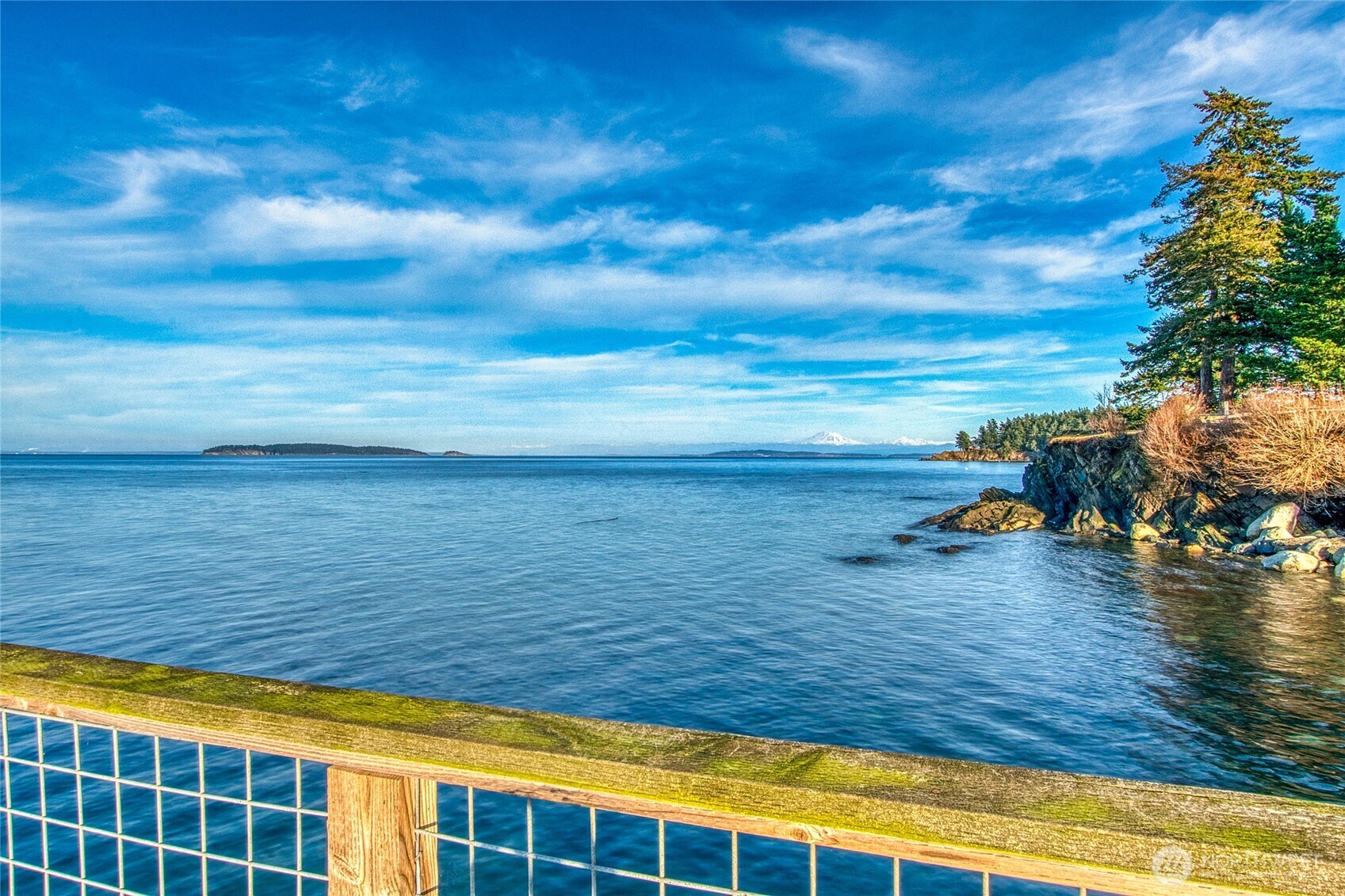 Waterfront view across the bay toward a wooded island and distant snow-capped mountains.