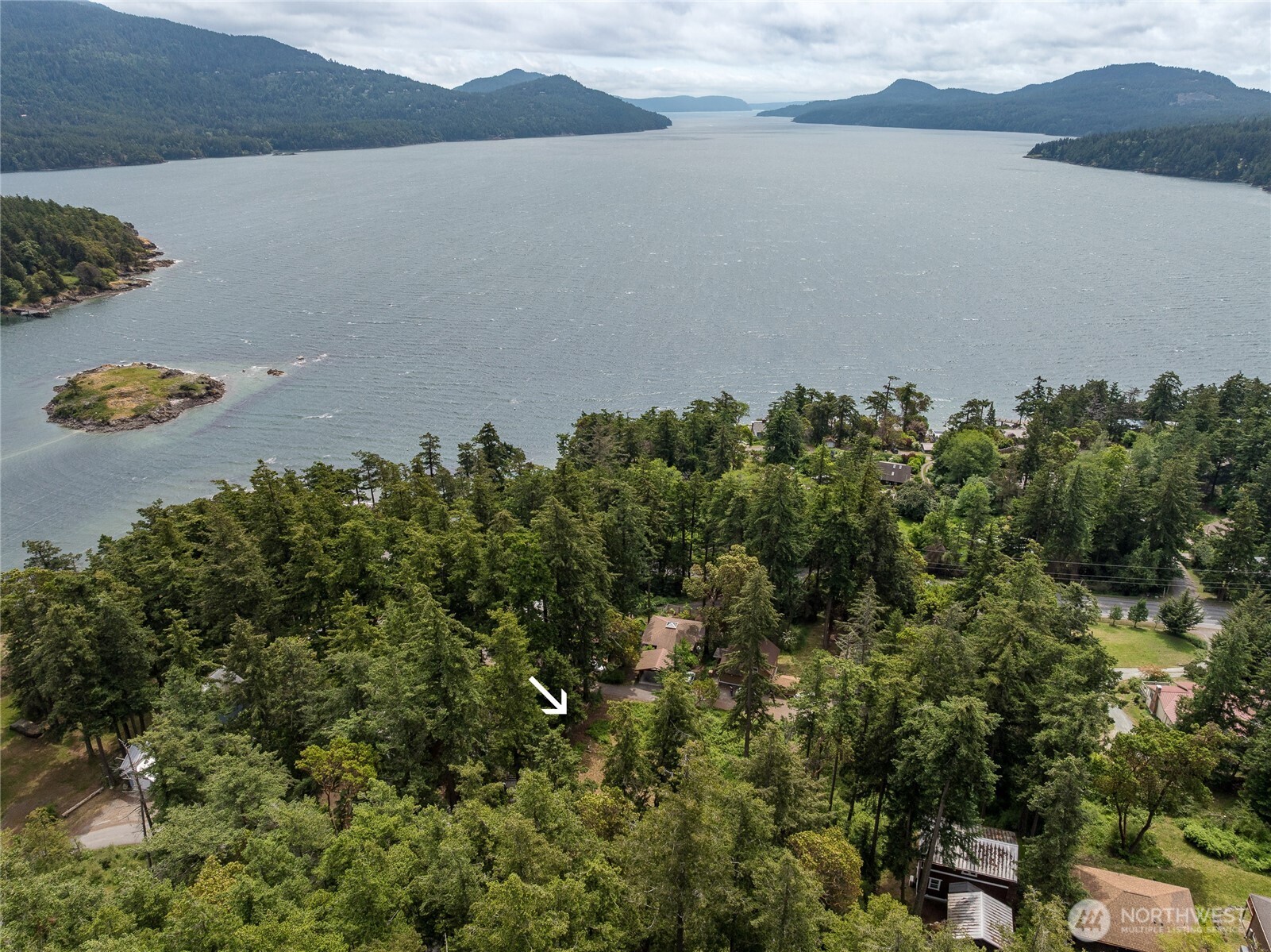Aerial view of a wooded property marked by a white arrow, with a broad bay and forested islands beyond.