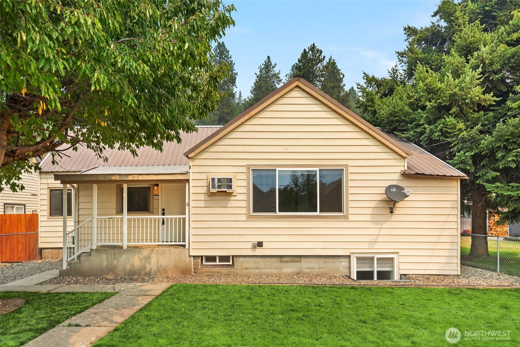 Pale yellow house with a covered porch, brown metal roof, and green front lawn.