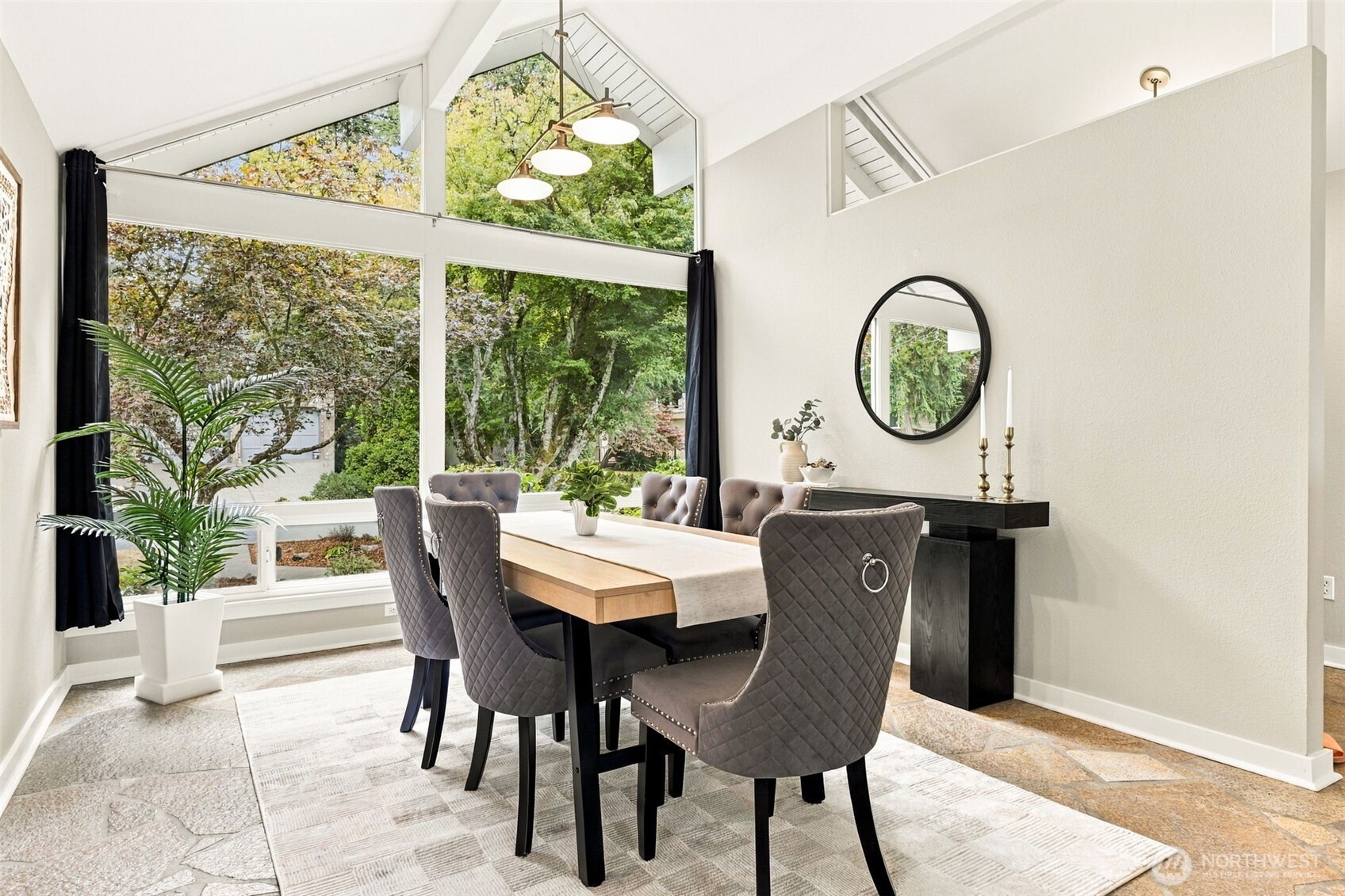 Dining room with a vaulted ceiling, large windows, and a wood table surrounded by gray chairs.