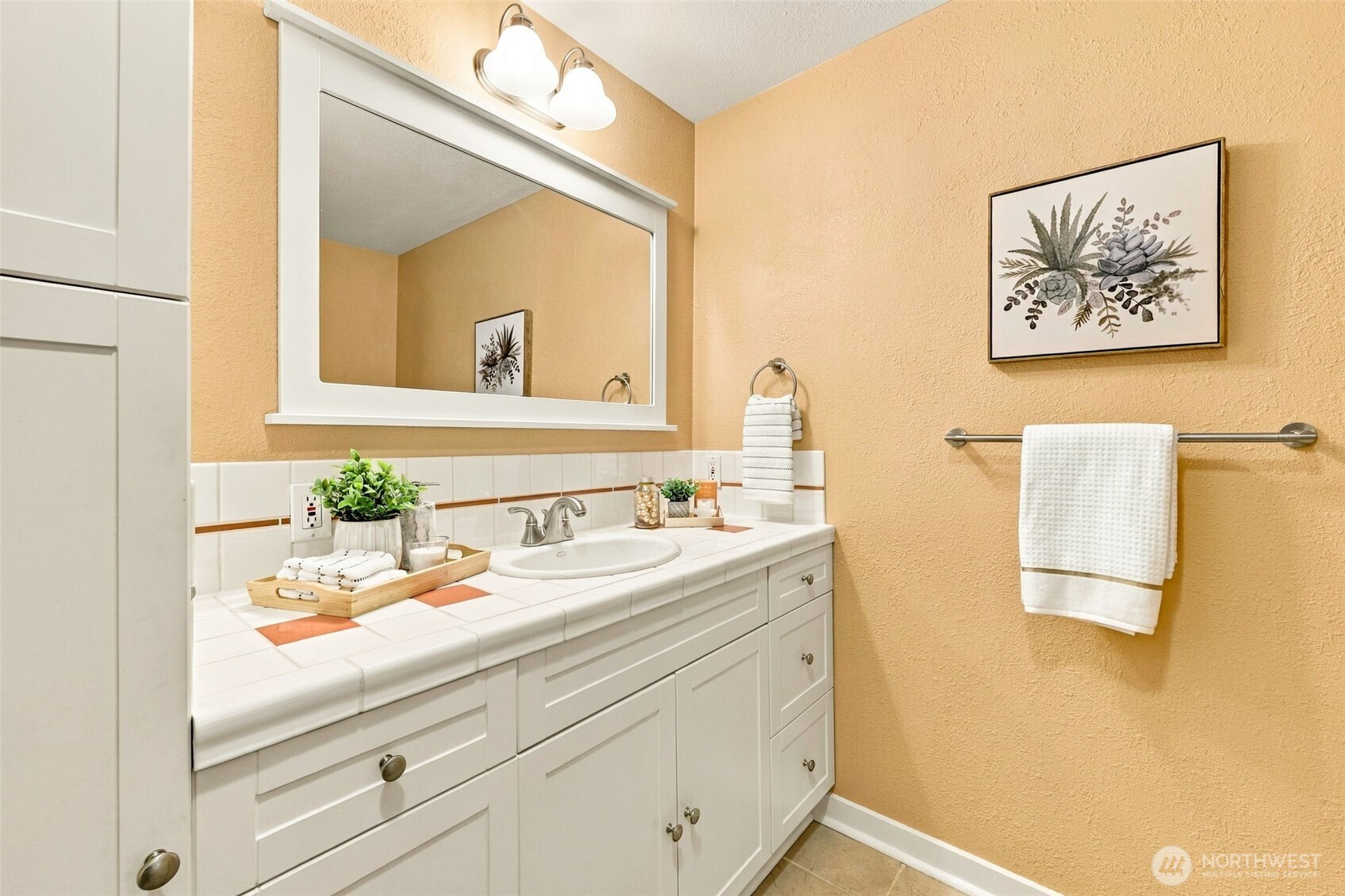 Staged bathroom with a white tiled vanity, large mirror, and peach-colored walls.