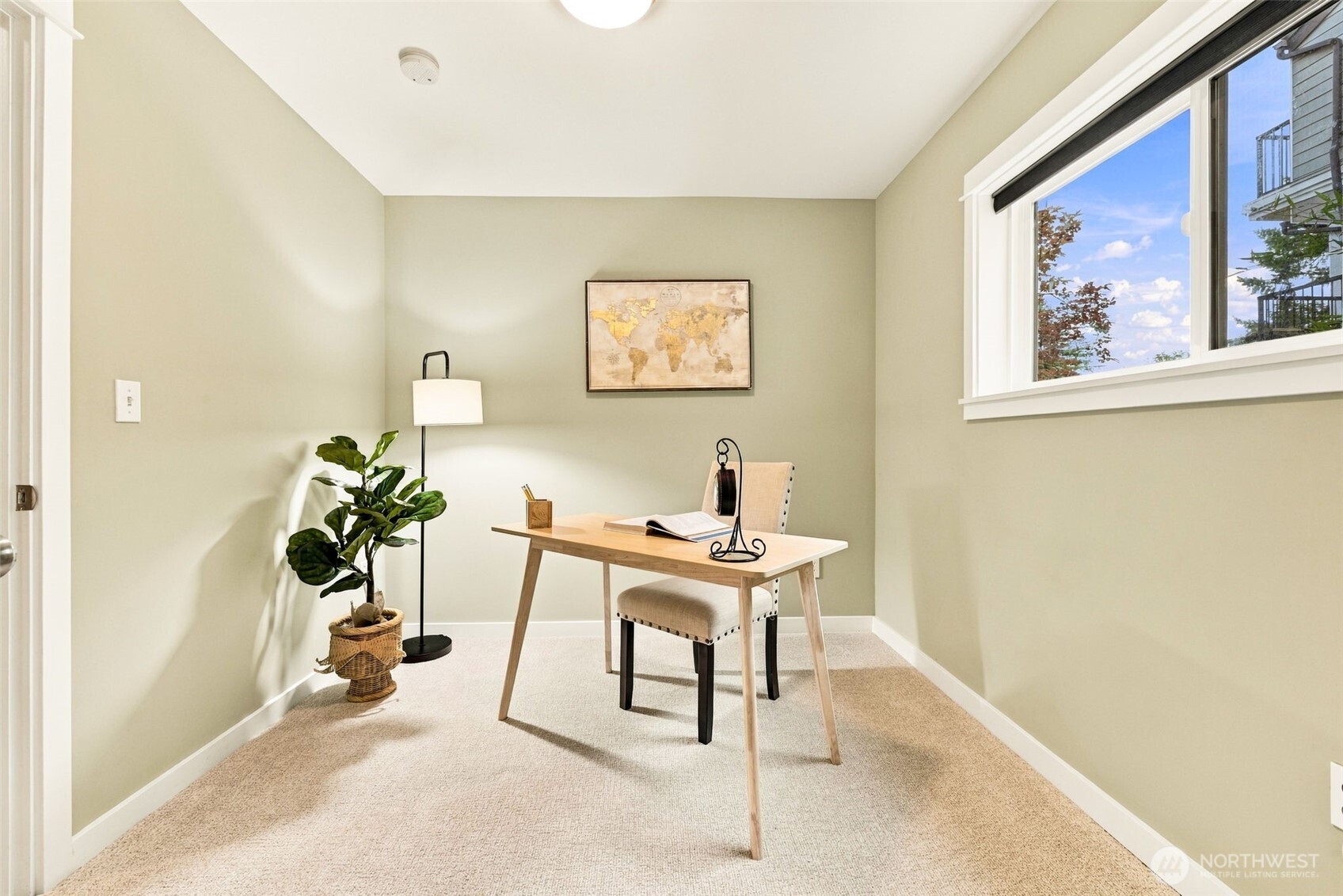 Staged home office with a light wood desk, upholstered chair, potted plant, and large window.