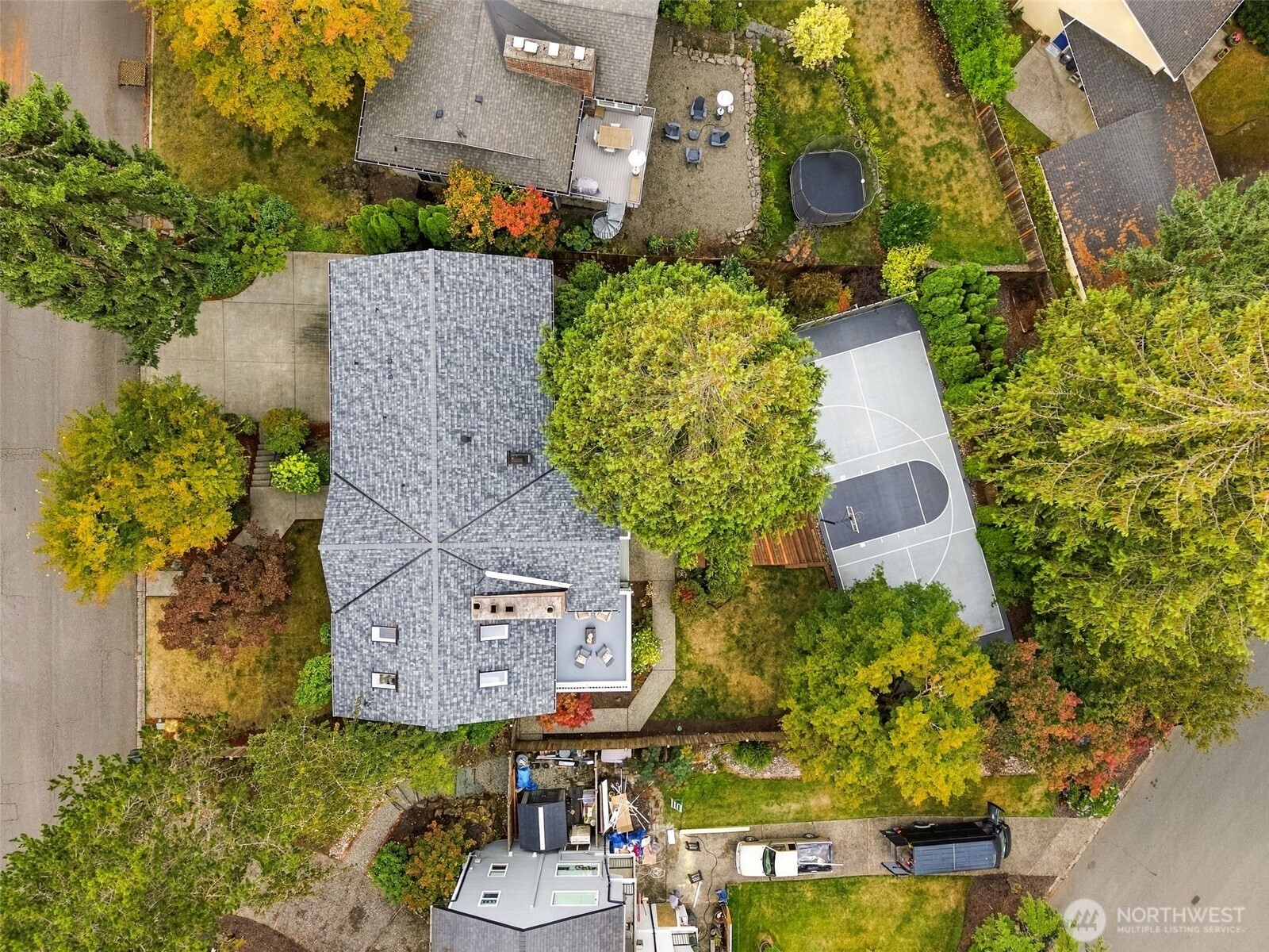 Aerial view of a home with a private basketball court, patio, and mature autumn trees.