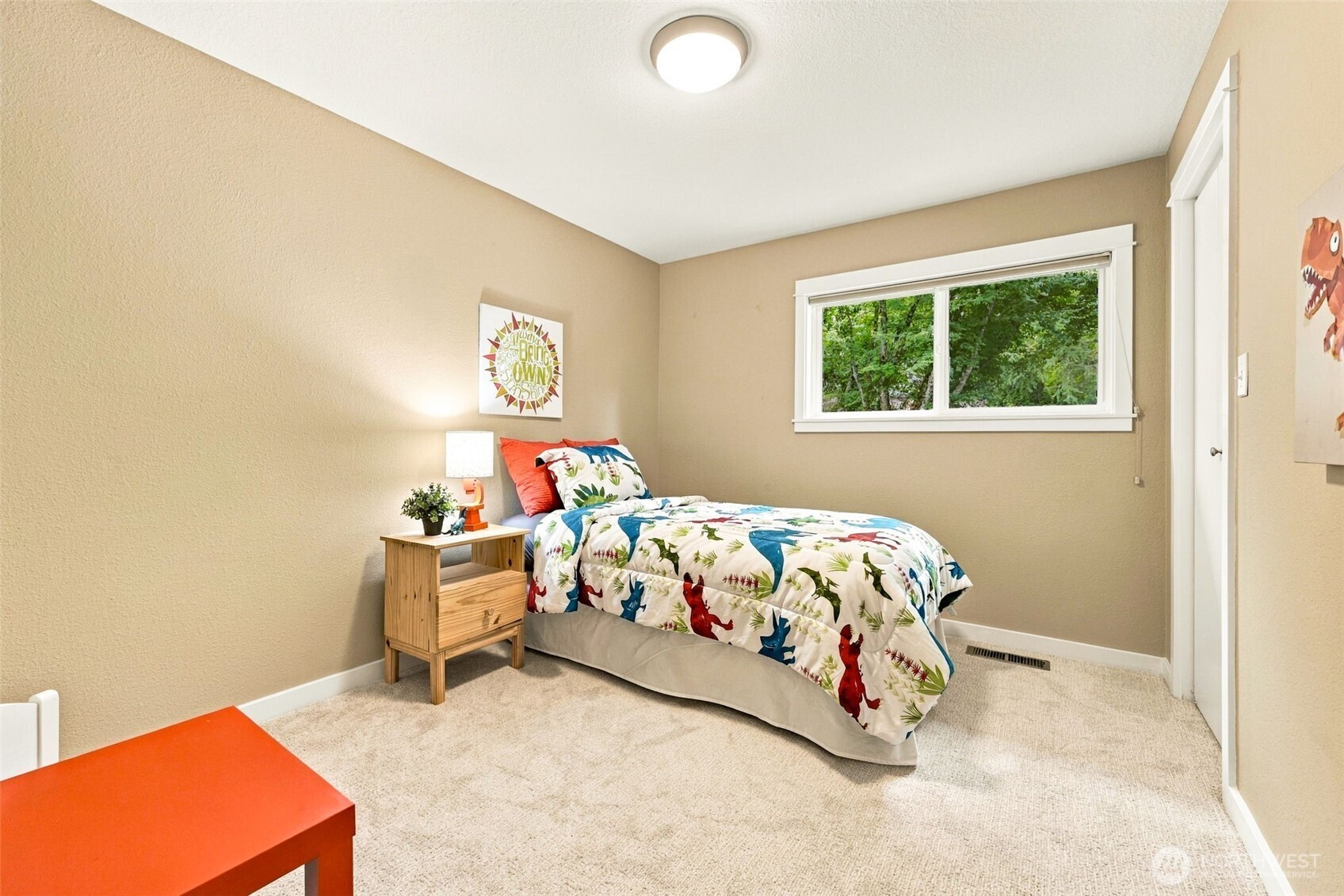 Furnished bedroom with colorful dinosaur-print bedding and a window overlooking trees.