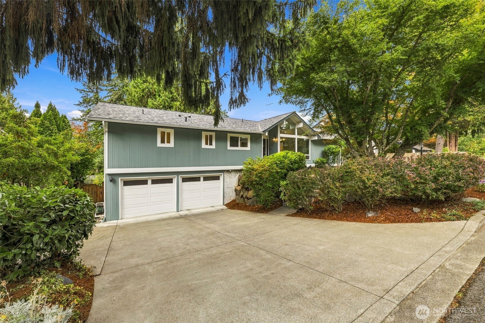 Blue-green house with a two-car garage, broad driveway, and mature landscaping.