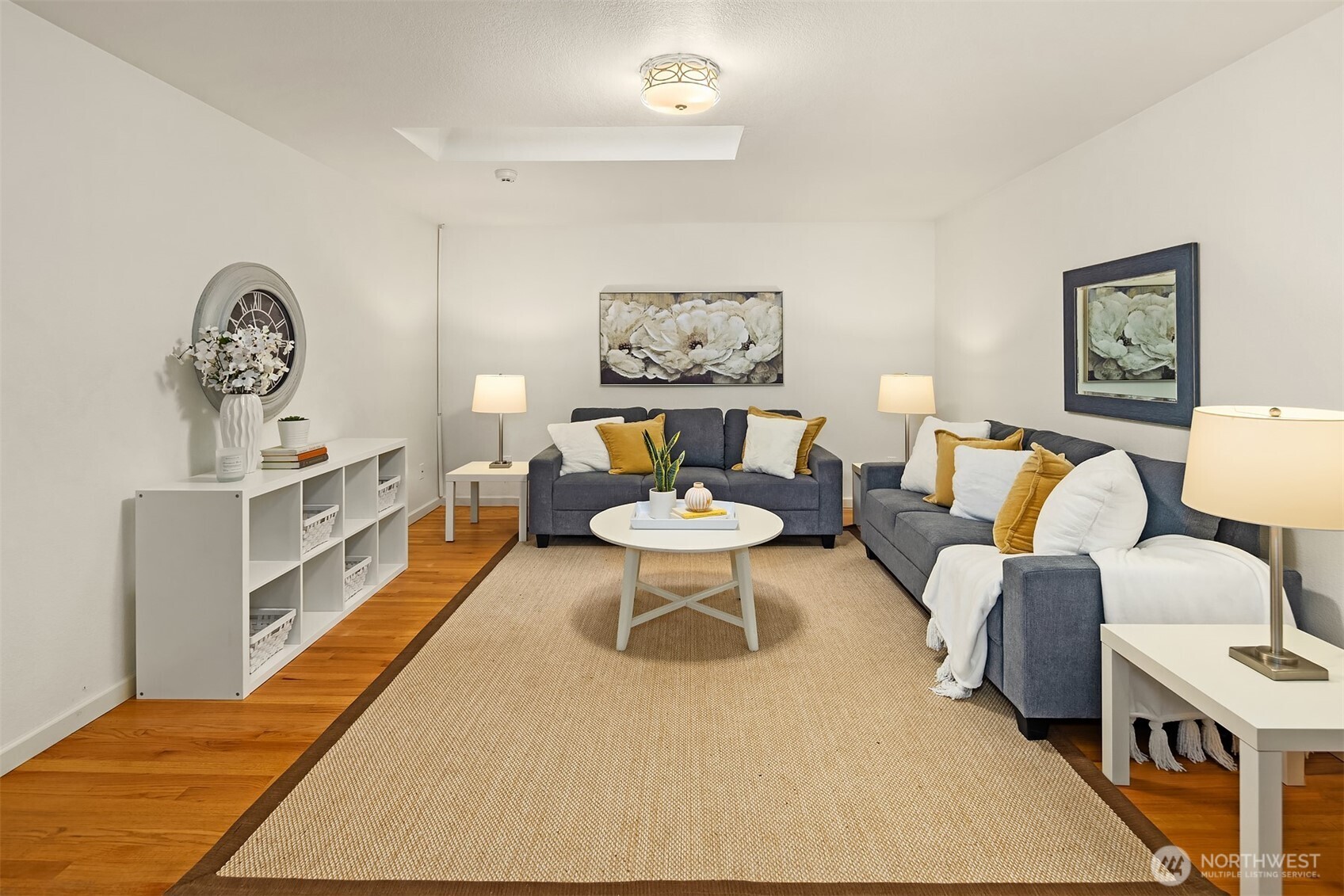 Staged living room with blue sofas, mustard cushions, a round coffee table, and hardwood floors.