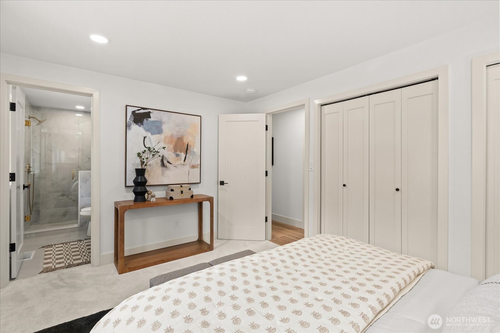 Staged bedroom with a patterned bedspread, wood console, and ensuite glass shower.