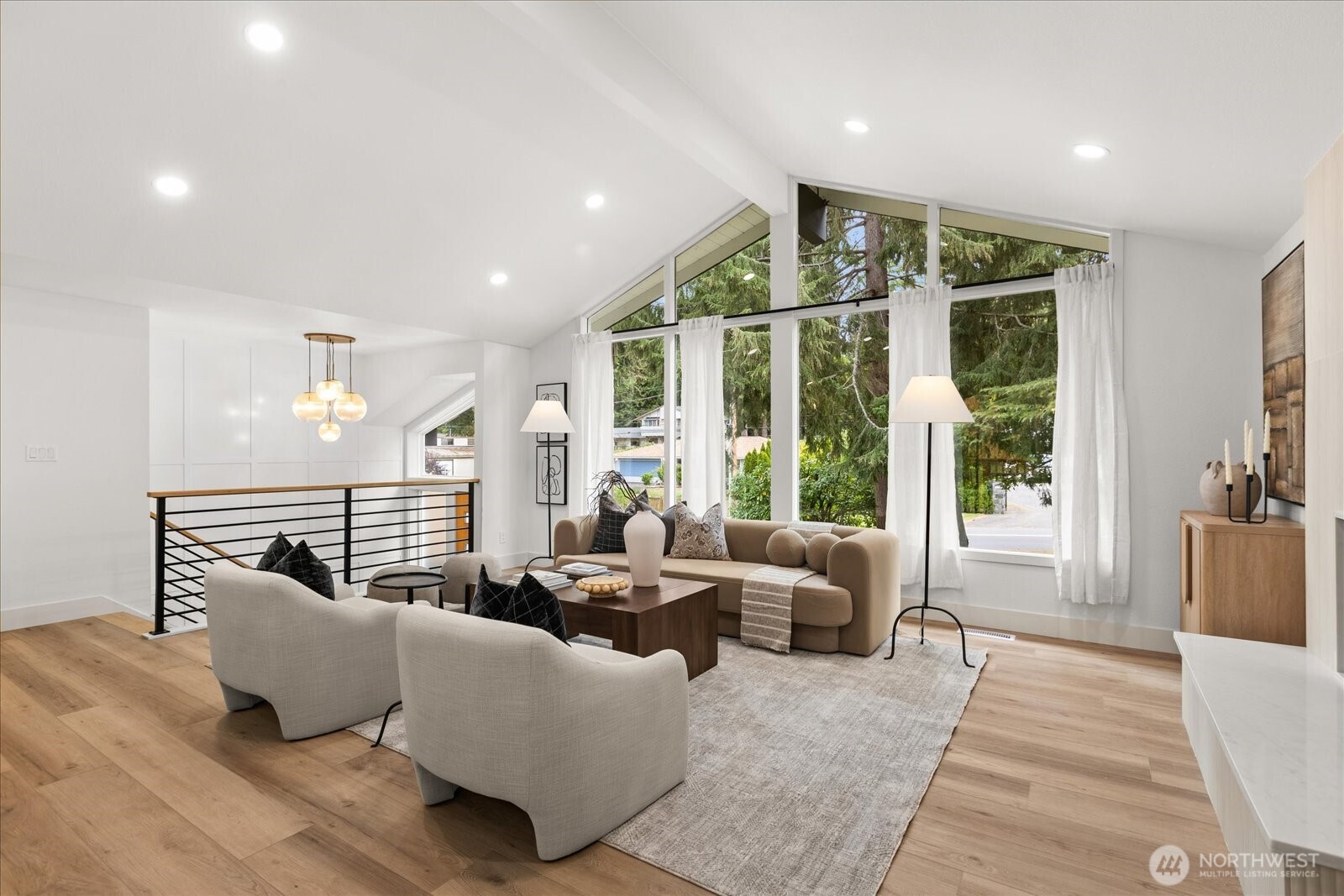 Furnished living room with vaulted ceiling, expansive windows, and views of evergreen trees.