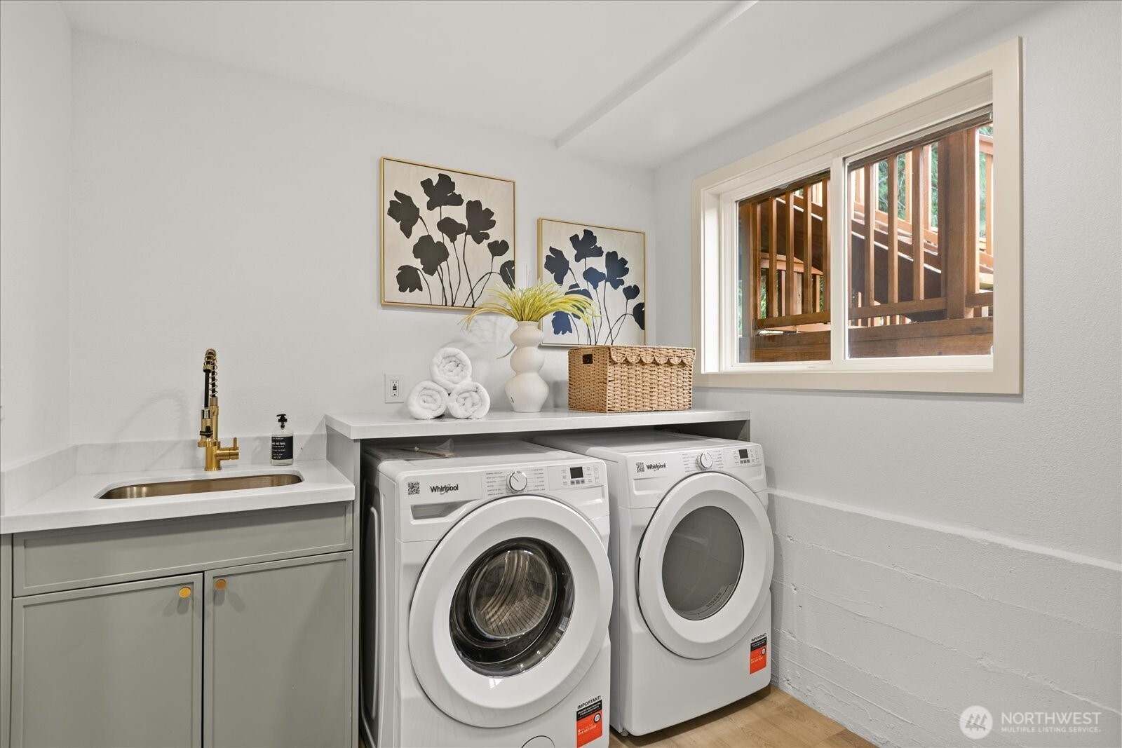Laundry room with front-loading washer and dryer, utility sink, and window overlooking a wooden deck.