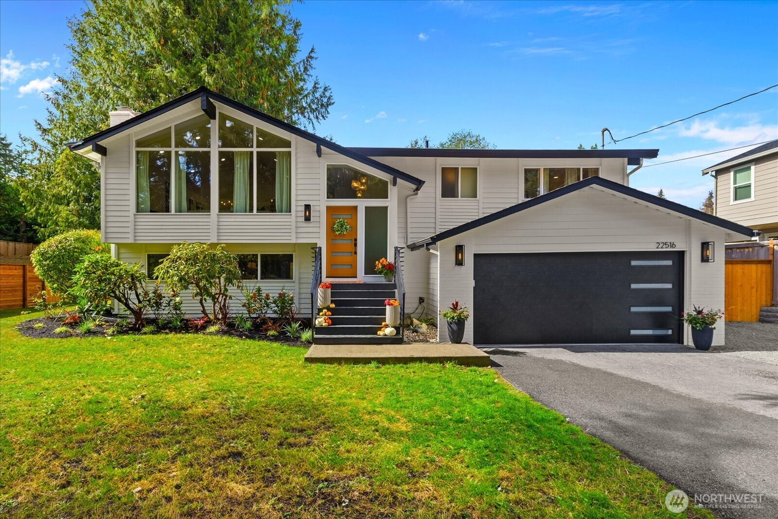 White split-level home with a tall gabled window, orange front door, and dark attached garage.