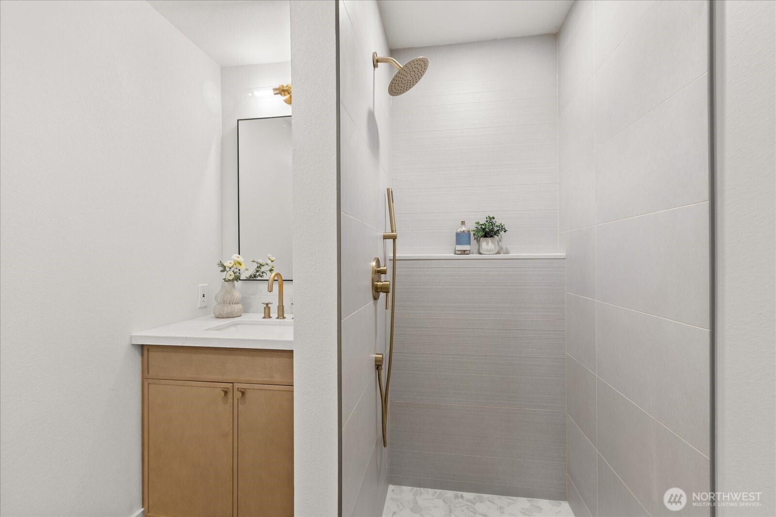 Bathroom with a tiled walk-in shower and brass fixtures beside a light wood vanity.