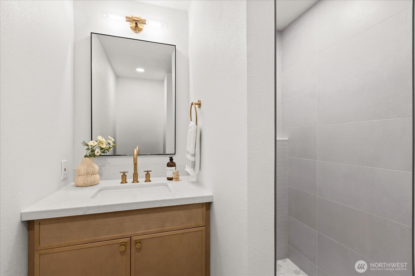 Bathroom vanity with gold fixtures beside a gray tiled shower.