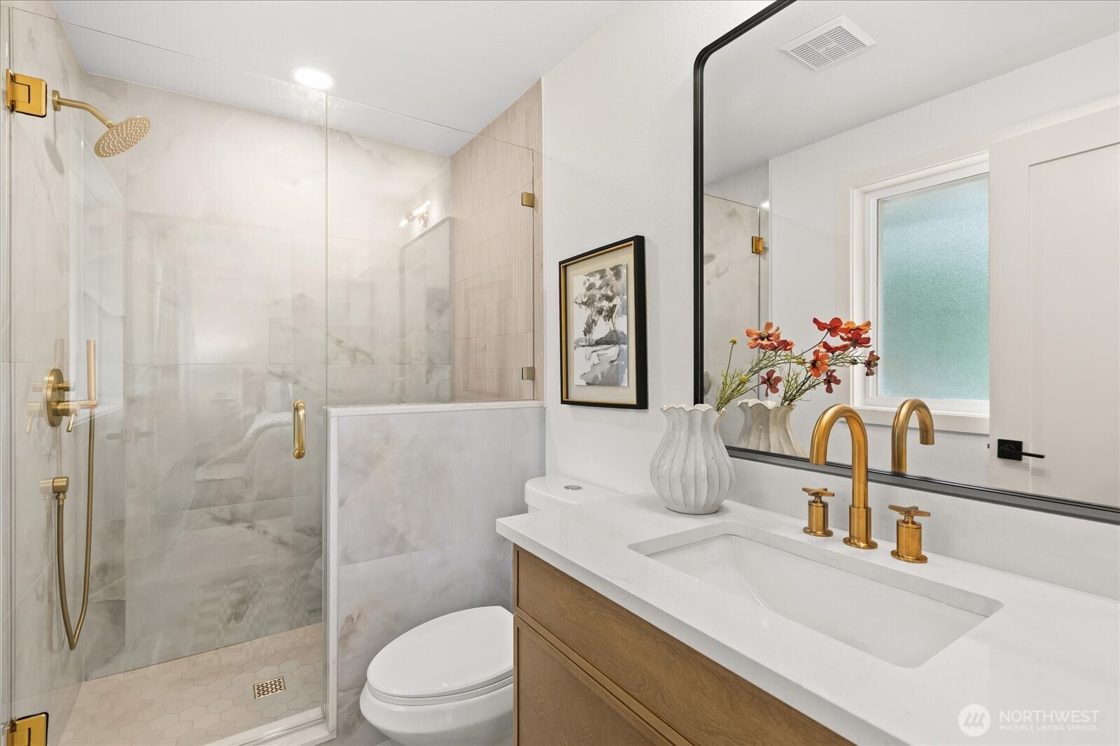 Bathroom with a glass walk-in shower, marble-look tile, and brass fixtures.