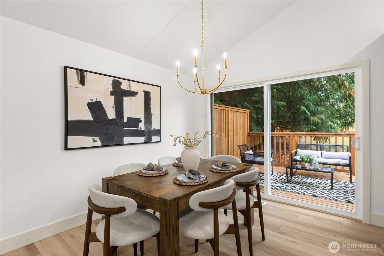 Dining room with a set table, gold chandelier, and sliding doors to a wooded deck.