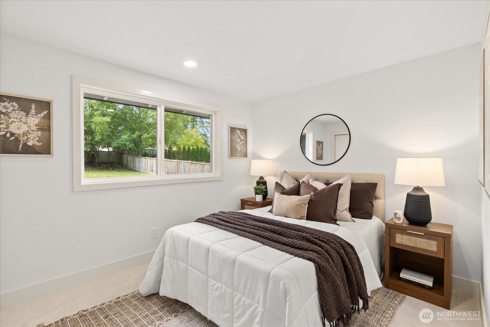 Staged bedroom with a white bed, dark throw, wood nightstands, and a large window overlooking the yard.