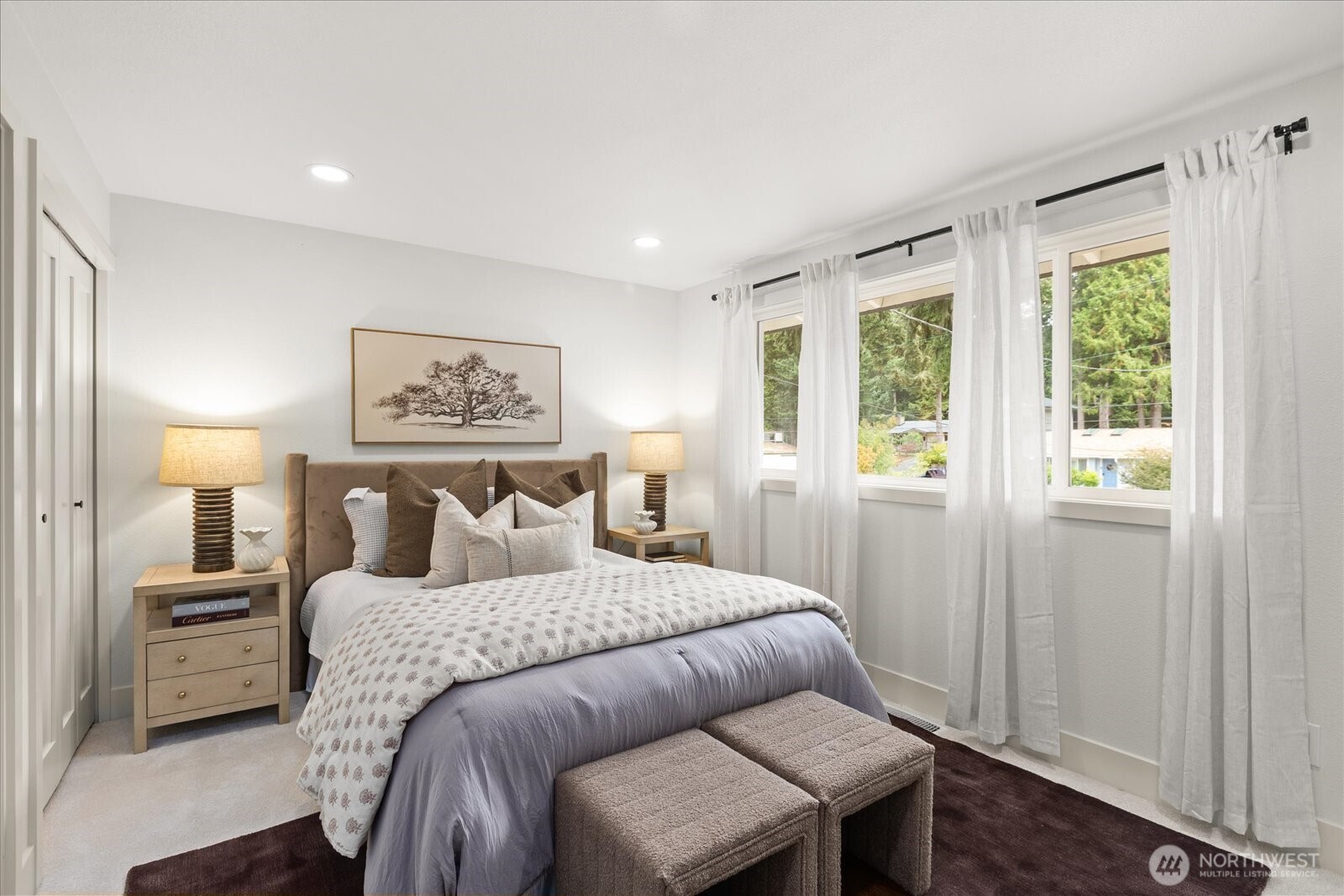 Staged bedroom with a large bed, neutral bedding, and tall curtained windows.